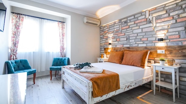 Un dormitorio con una cama blanca, dos sillas azules, una mesita de noche de madera y una pared con diseño de ladrillo.