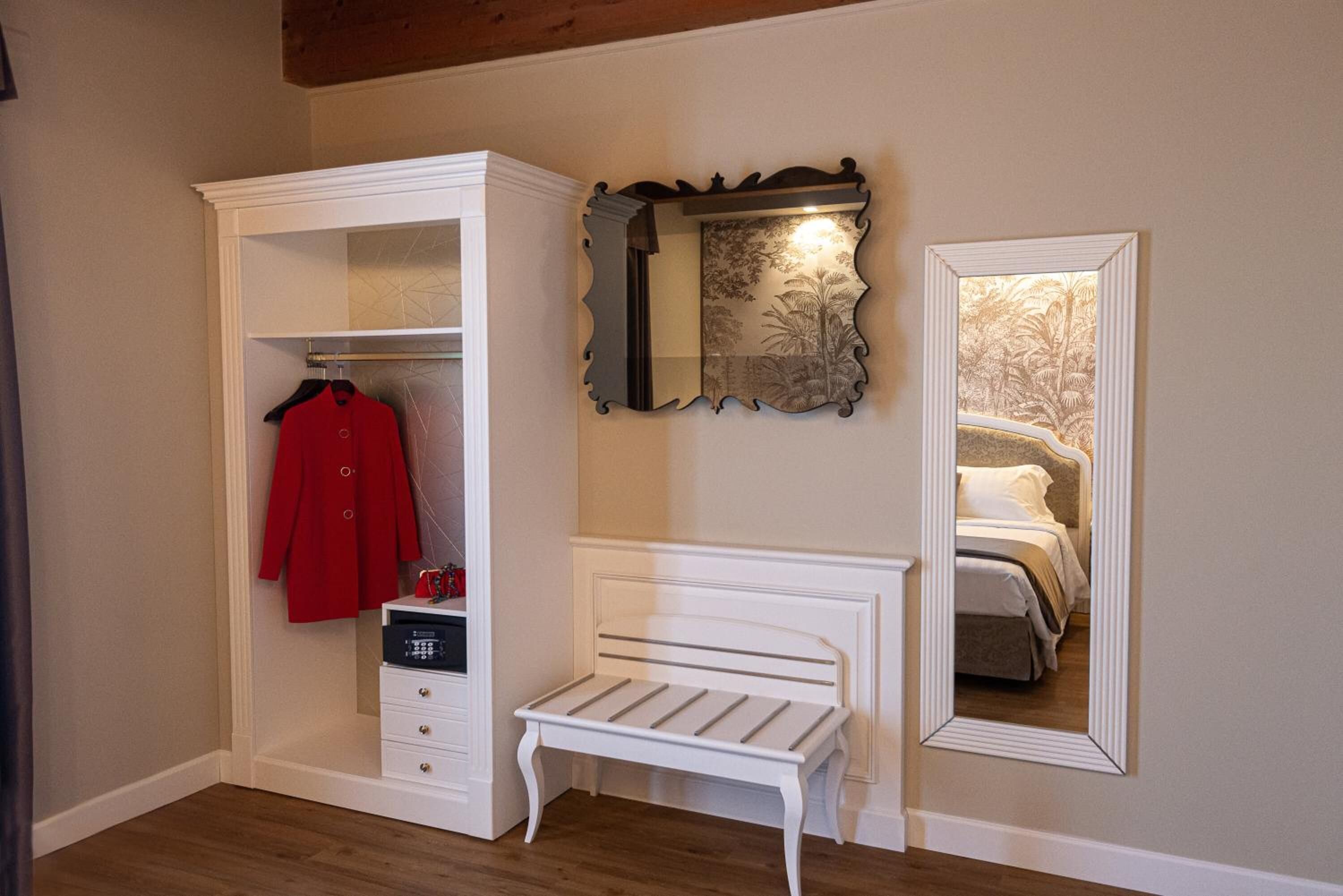 Ein Schlafzimmer mit einem weißen Bett, einer weißen Bank, einem Kleiderschrank und einem Spiegel.