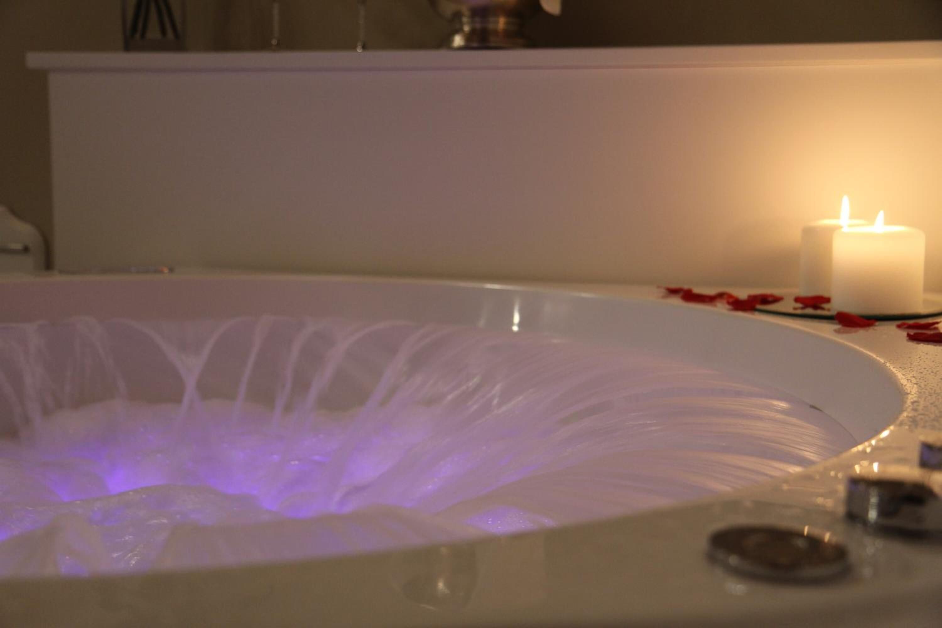 A bathtub with a water fountain feature, a lit candle, and rose petals on the edge.
