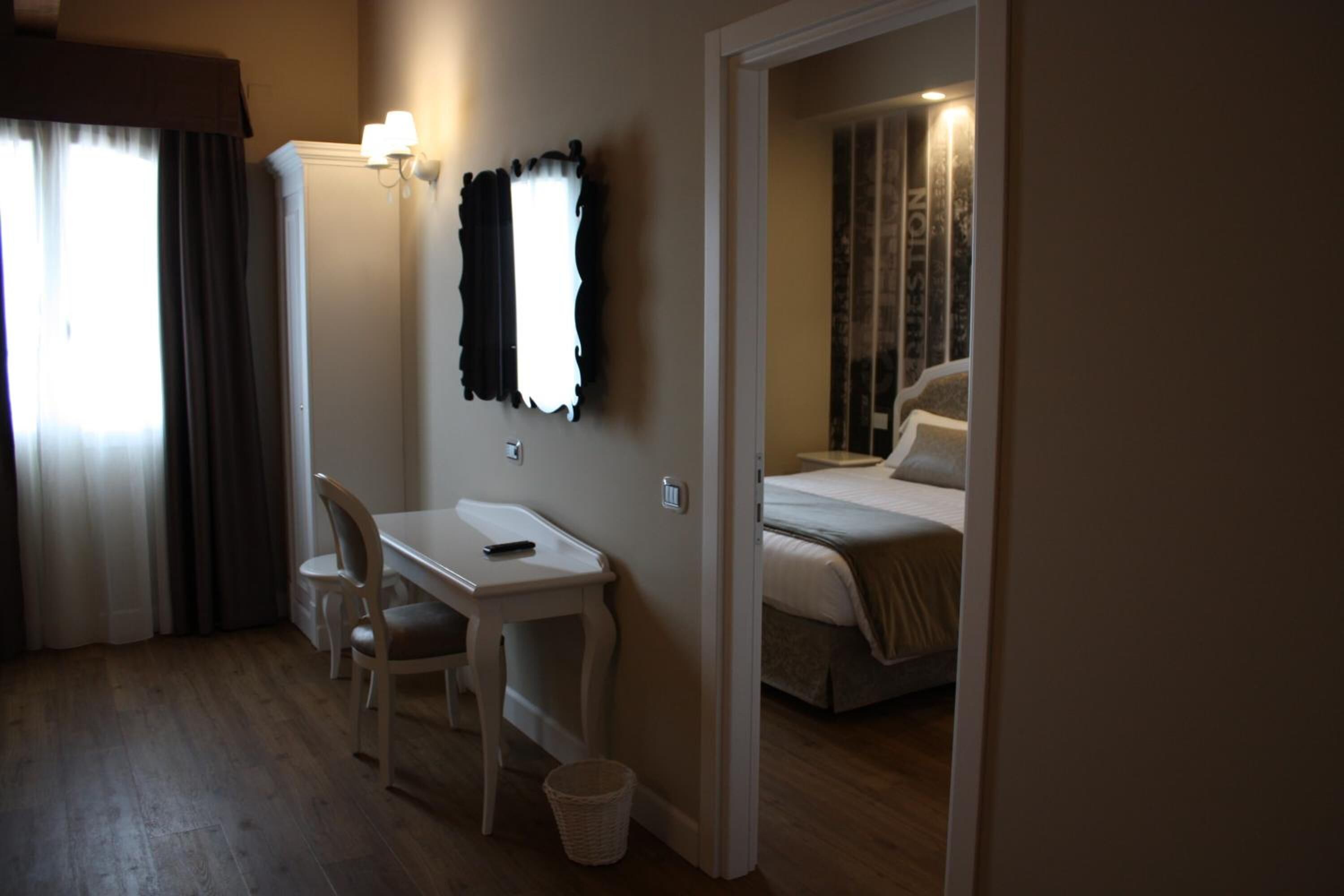 Habitación de hotel con cama, escritorio, silla, lámpara y ventana con cortinas.