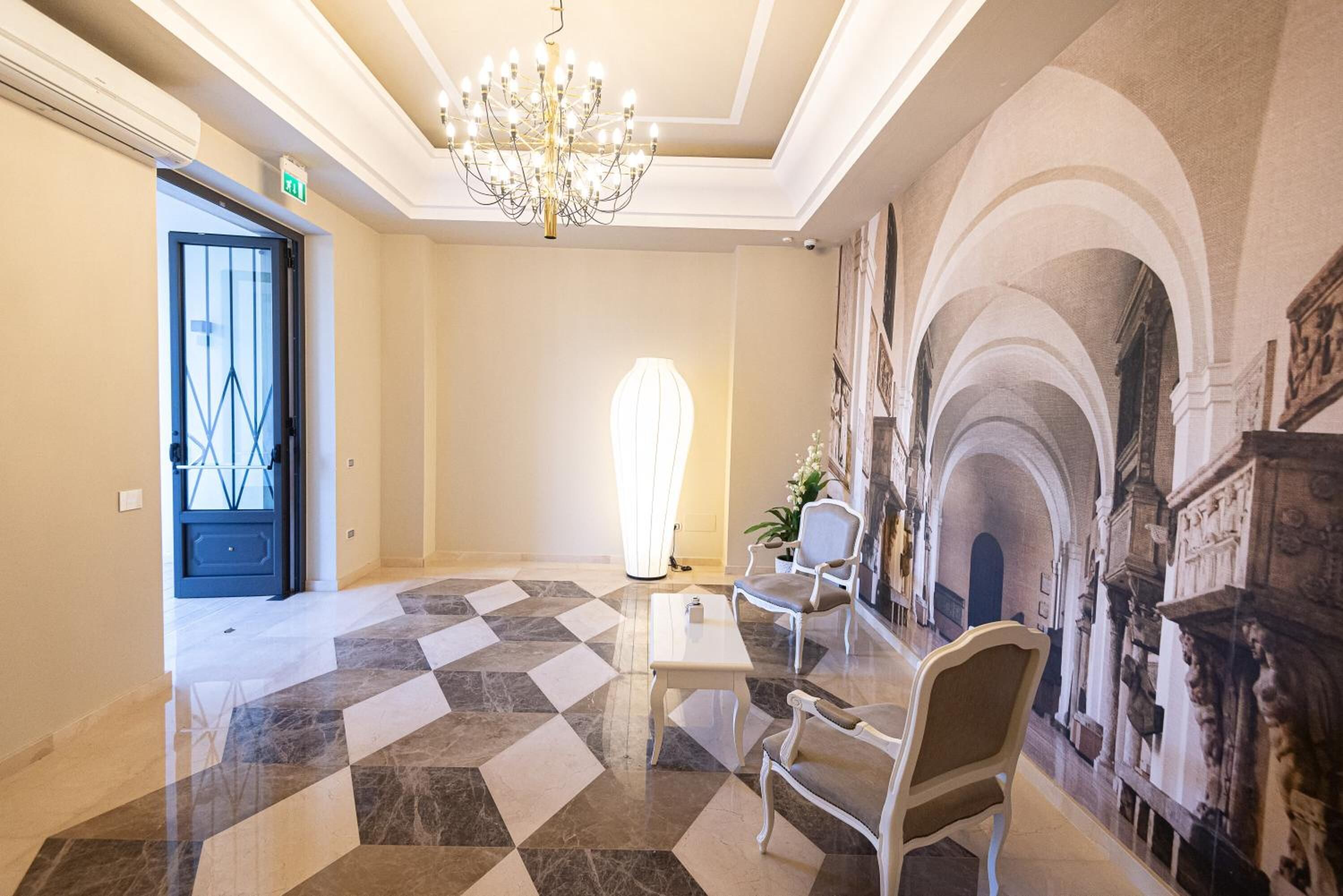 A spacious lobby with a checkered floor, a chandelier, and a seating area with chairs.
