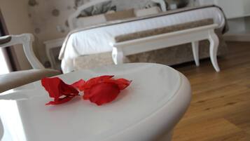 A white table with red rose petals in a room with a bed and white furniture.