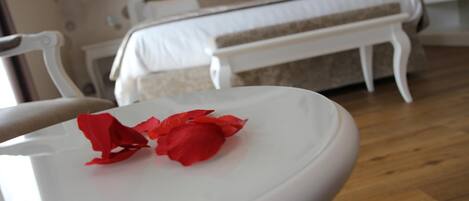 A white table with red rose petals in a room with a bed and white furniture.