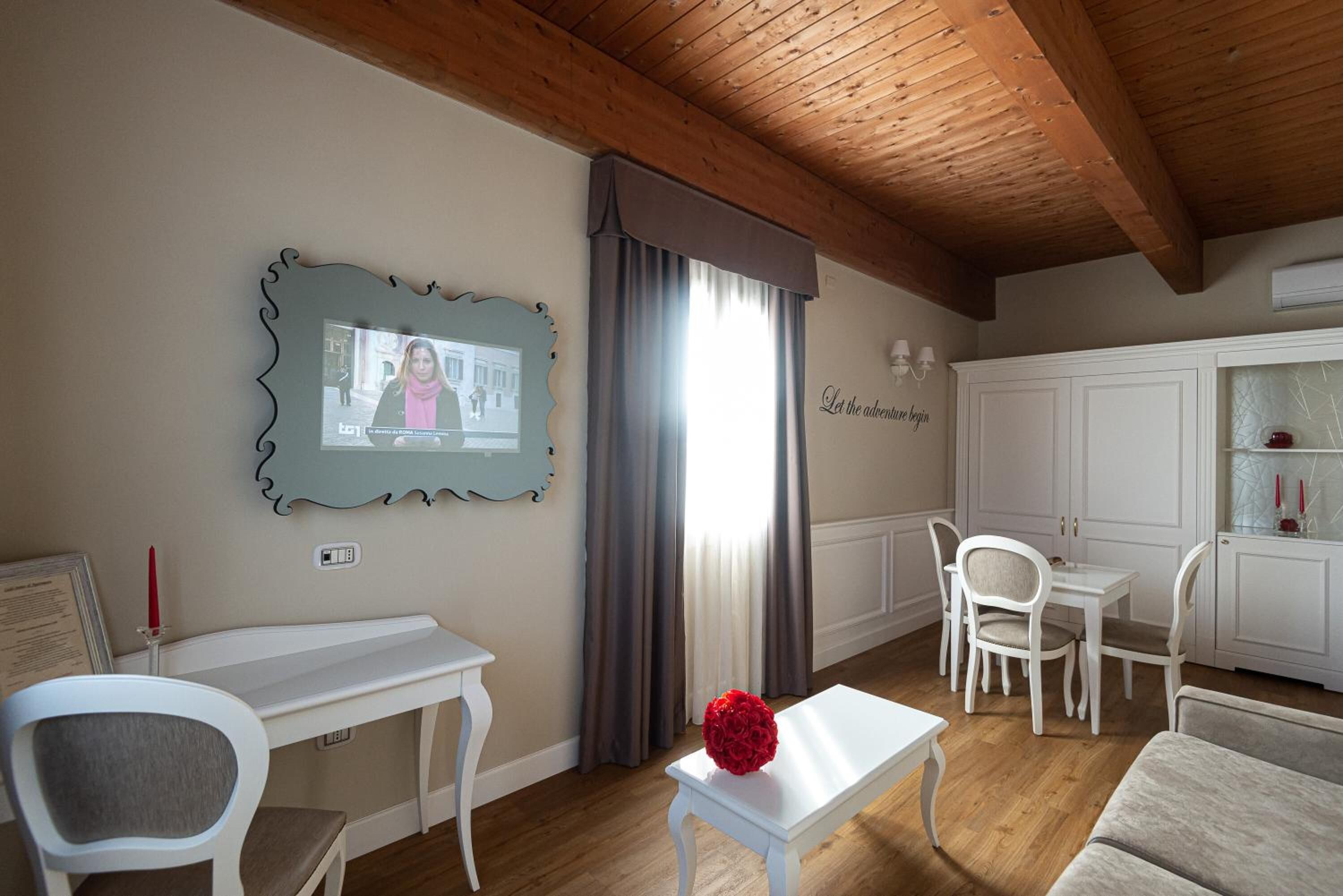 Una habitación con techo de madera, un escritorio blanco, una silla blanca, una mesa blanca con una flor roja y un armario blanco.