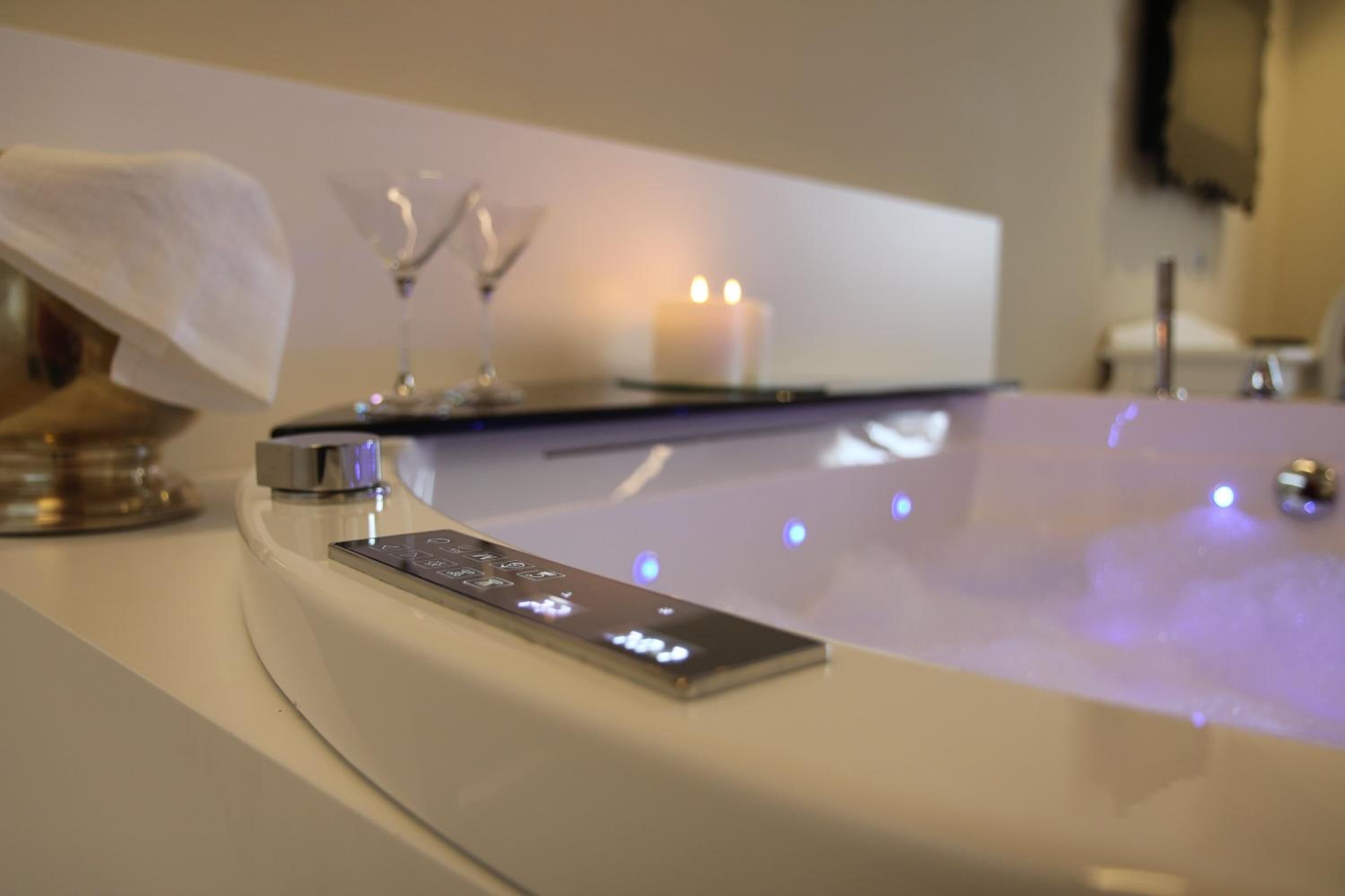 A modern bathroom with a digital control panel, a white bathtub, and a candle on the edge.