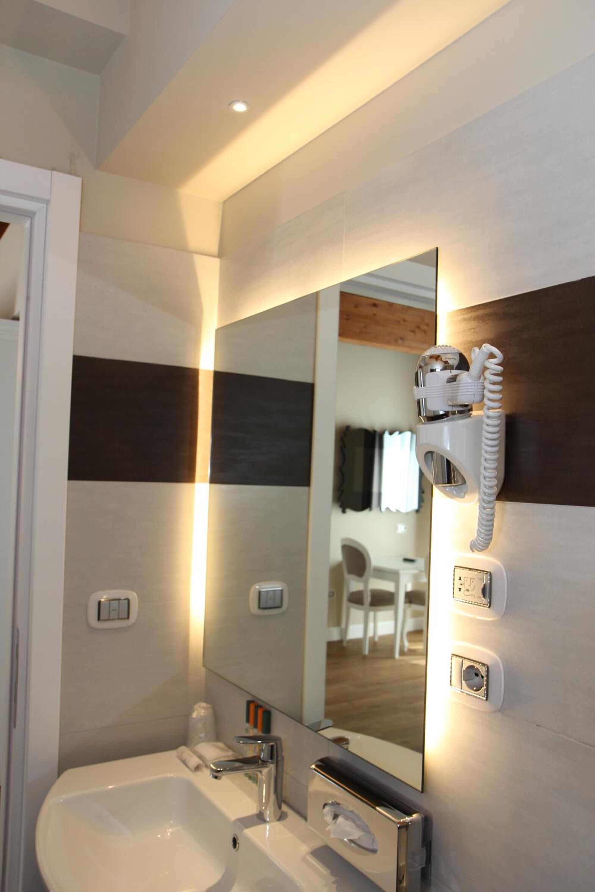 A modern bathroom with a large mirror, a built-in sink, a hairdryer, and a telephone.