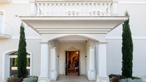 A grand entrance with a white balustrade, two tall columns, and a covered walkway leading to a door with a glass door and a chair inside. - Suites&Apartments Liolà (Castrocielo)