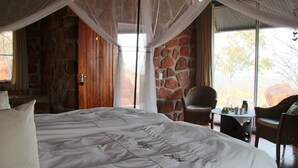 A bedroom with a large bed, stone walls, and a view of the outdoors. - Waterberg Wilderness (Waterberg)