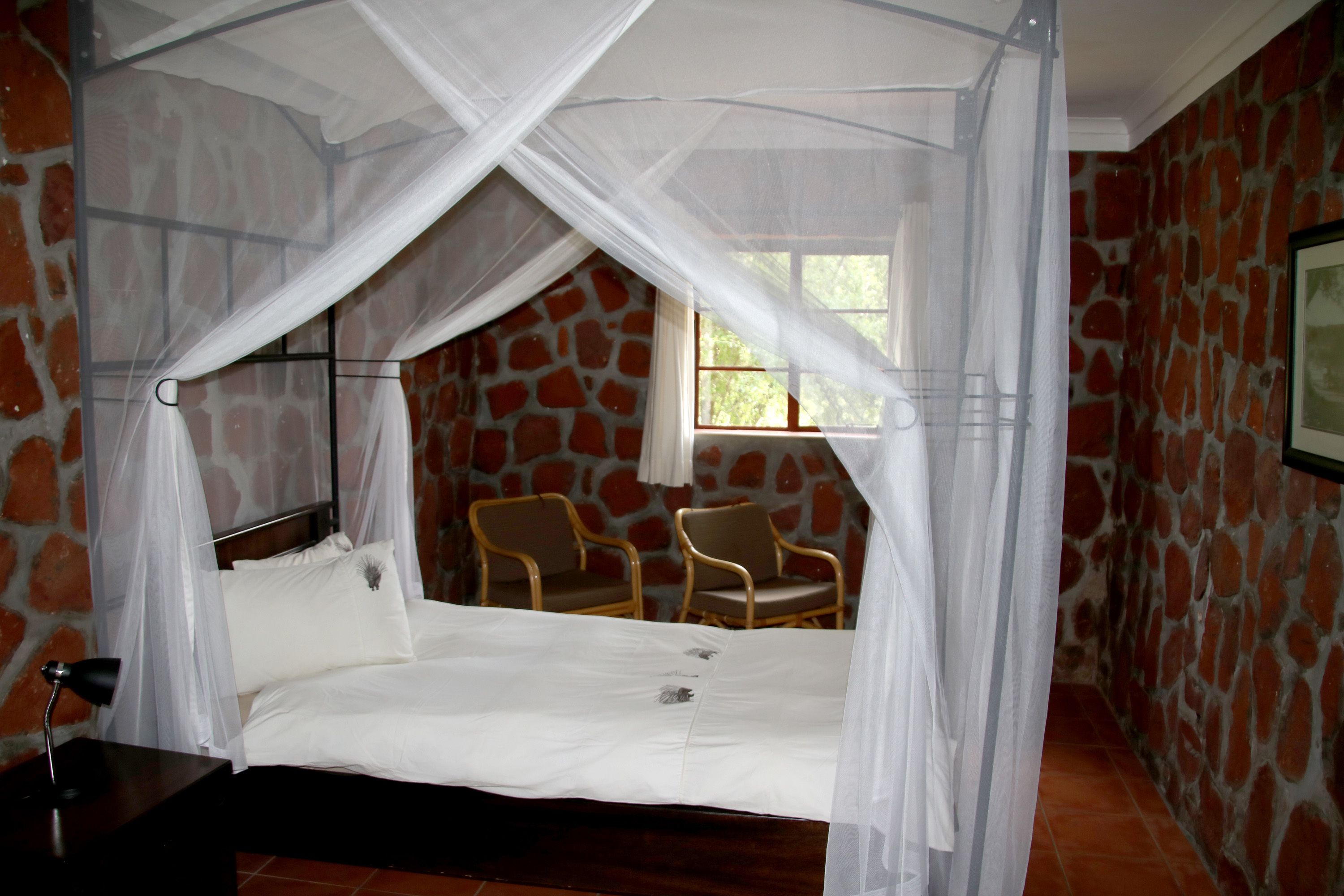 A bed with a canopy, two chairs, and a stone wall.