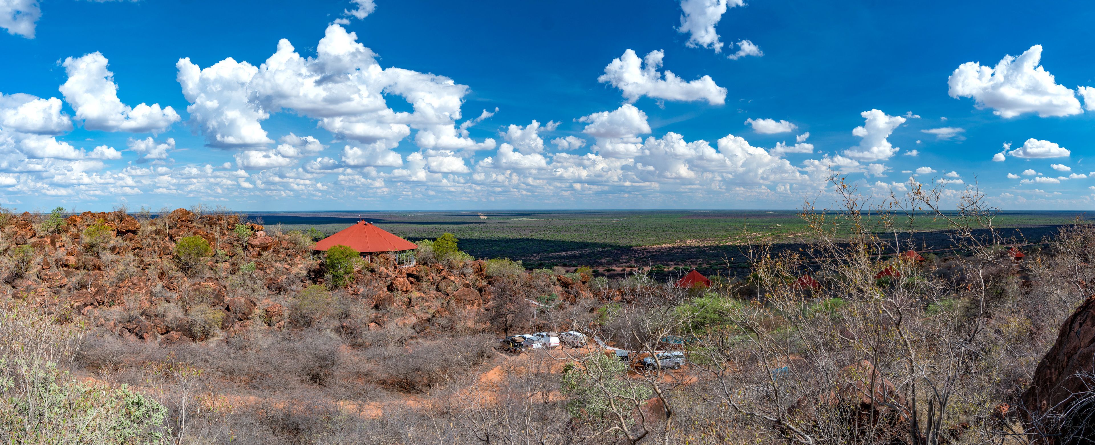 Un paysage comprenant un bâtiment à toit rouge, un chemin de terre et une végétation clairsemée.