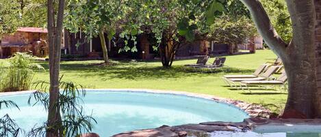 A swimming pool surrounded by a grassy area with trees and a building in the background.