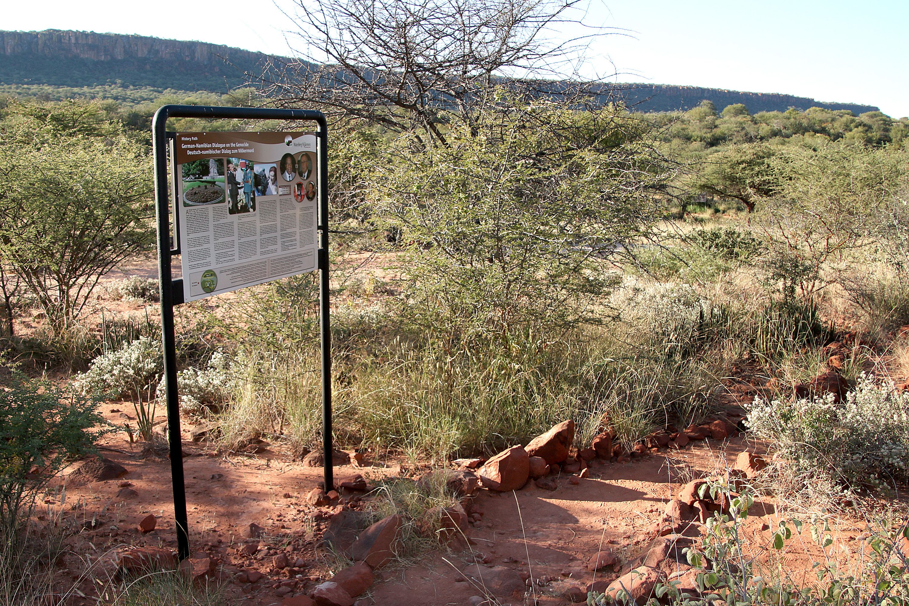 Ein Schild in einer natürlichen Umgebung mit spärlicher Vegetation und einer Berglandschaft im Hintergrund.