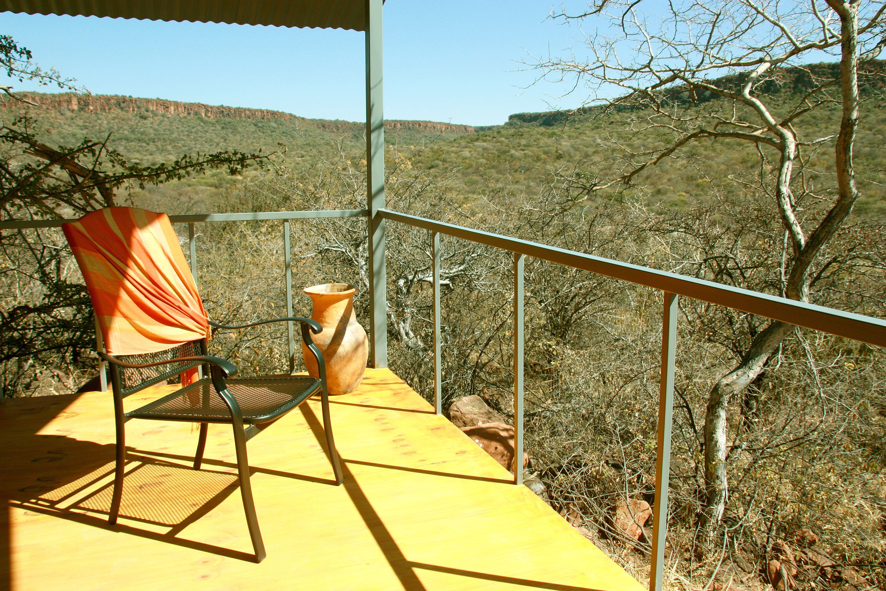 Un balcón con una silla y un florero, con vistas a un paisaje montañoso.