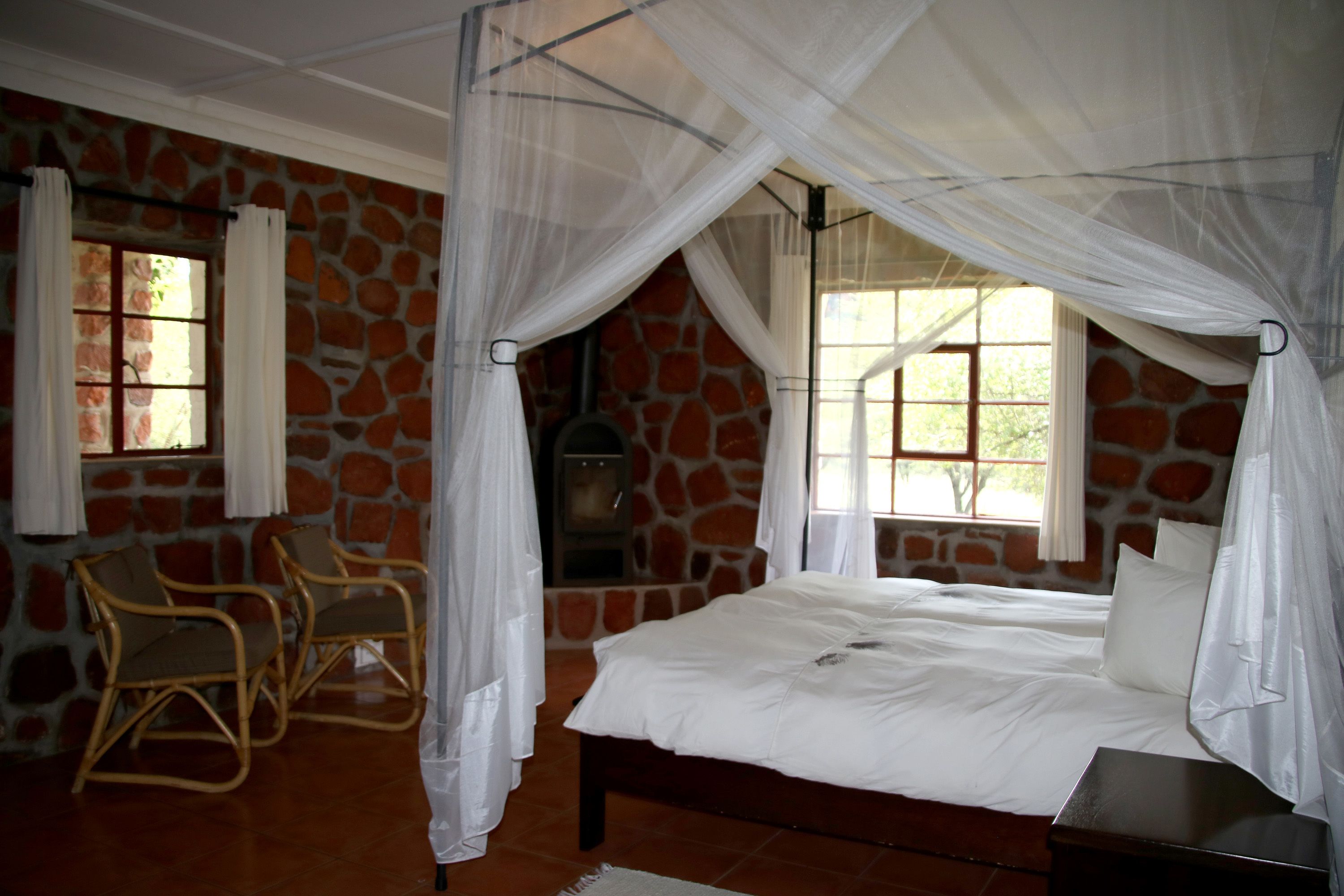 A bedroom with a stone wall, a bed with white bedding, a wooden nightstand, and a chair.