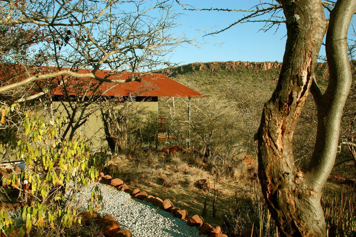 Ein Haus mit rotem Dach, umgeben von einem Kiesweg und spärlicher Vegetation.
