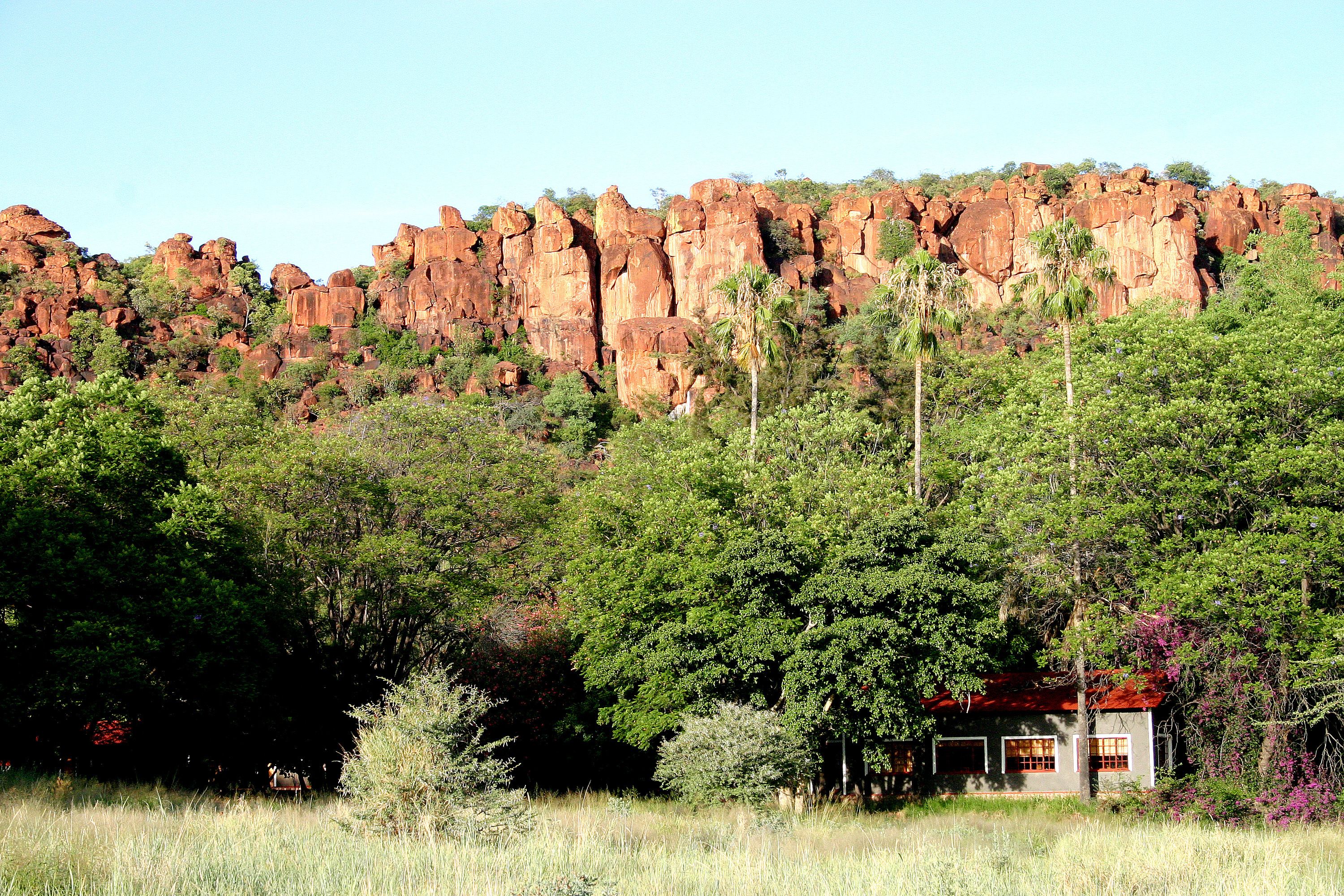 A house with a red roof nestled among trees and red rock formations in the background.