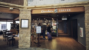 Interior de una cafetería con pared de piedra, techo de madera y un letrero que dice "Caribou Coffee".