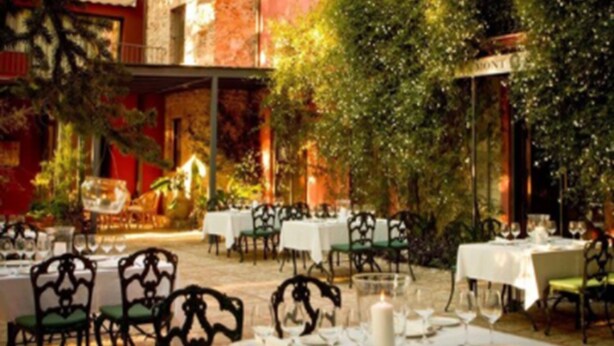 An outdoor dining area with tables and chairs, surrounded by greenery and a brick wall. - Mont-Sant Hotel (Xàtiva)