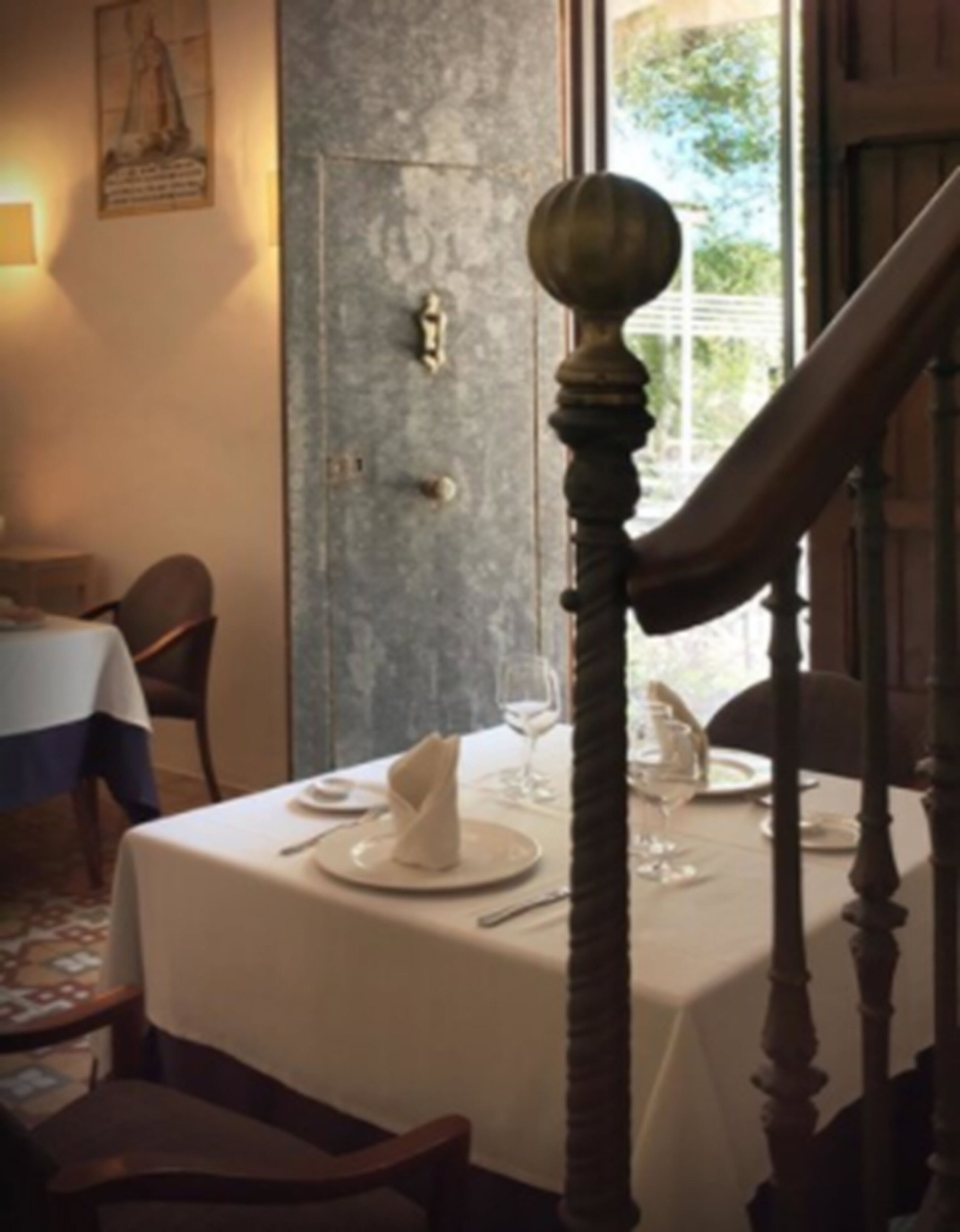 A dining area with a table set for two, a staircase, and a door with a light switch.