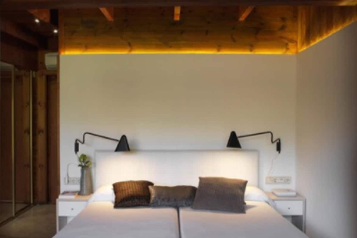 A double bed with two bedside tables, each with a lamp, in a room with wooden ceiling beams and white walls.