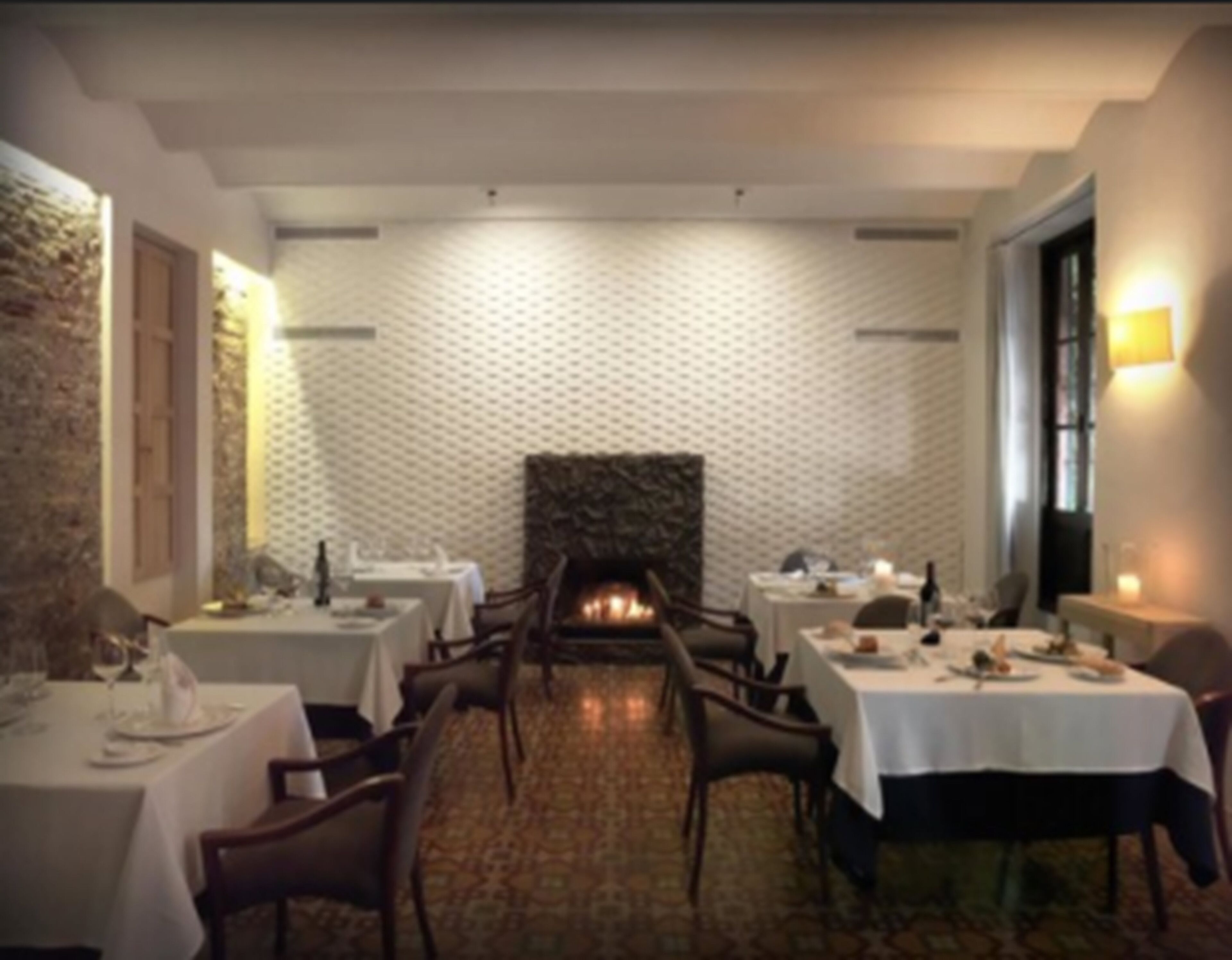 A restaurant with multiple tables and chairs, a fireplace, and a patterned wall.