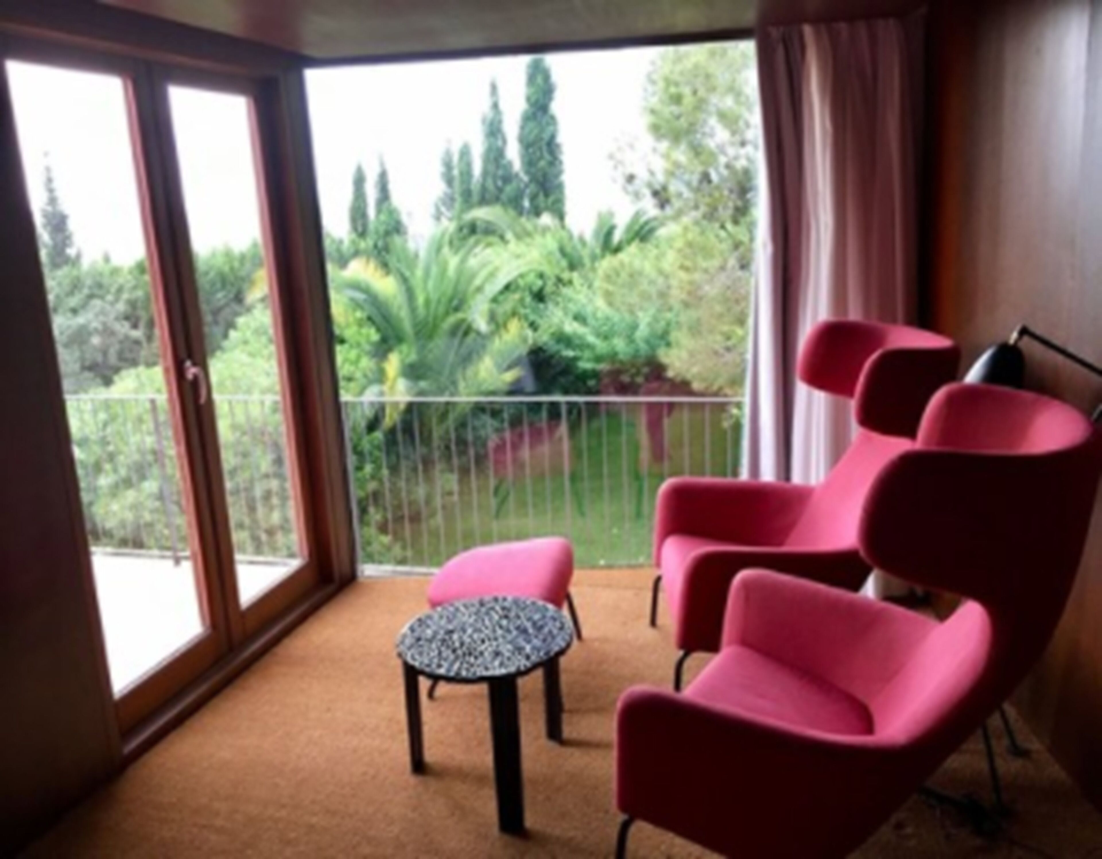Un balcón con vistas a follaje, dos sillas rosadas y una pequeña mesa redonda.