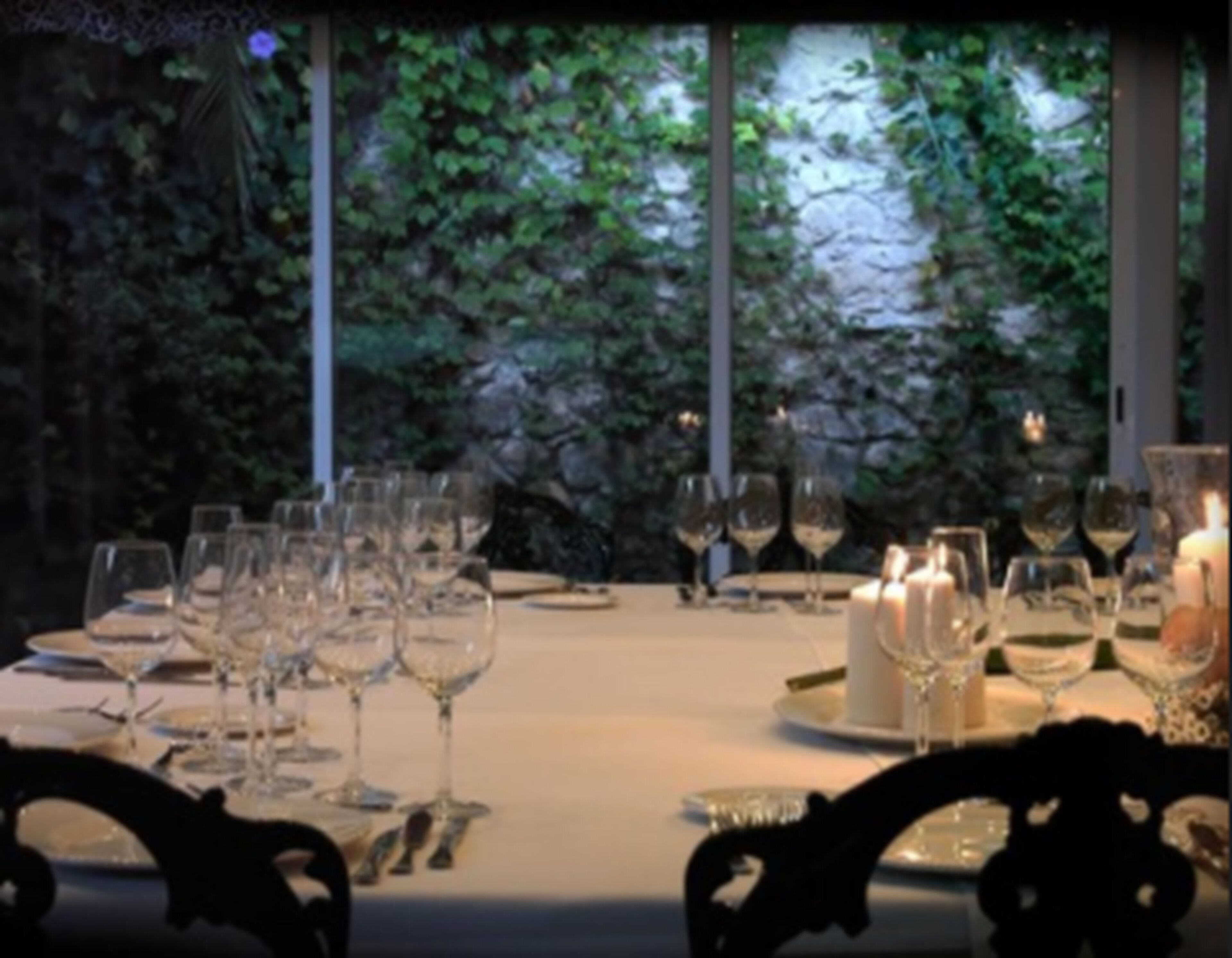 A dining table set with wine glasses and candles, surrounded by chairs.