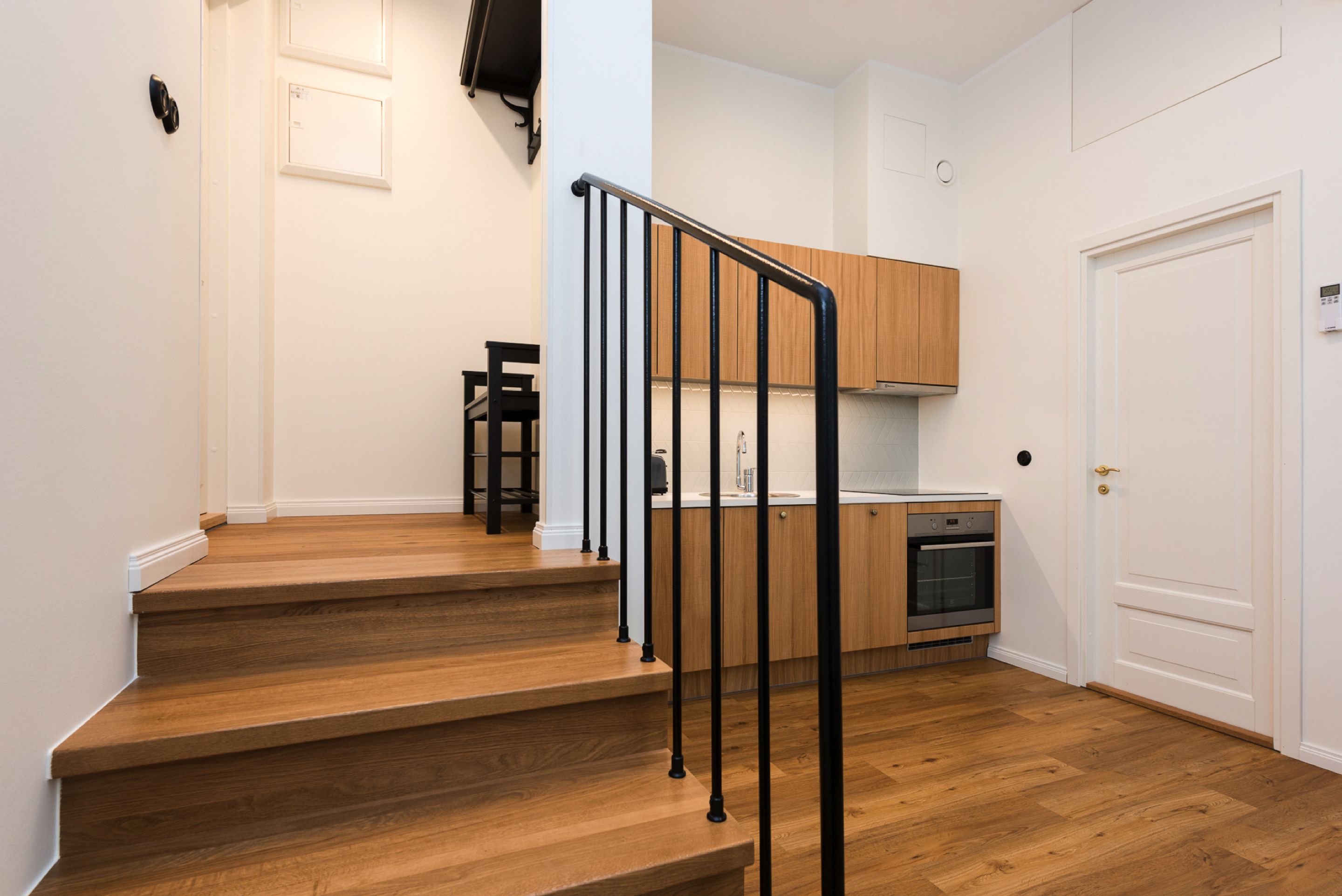 A staircase with wooden steps and black railings leading to a kitchen area with wooden cabinets and a built-in oven.