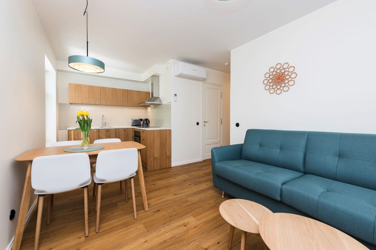 A modern kitchen with wooden cabinets, a dining table with chairs, and a blue sofa.