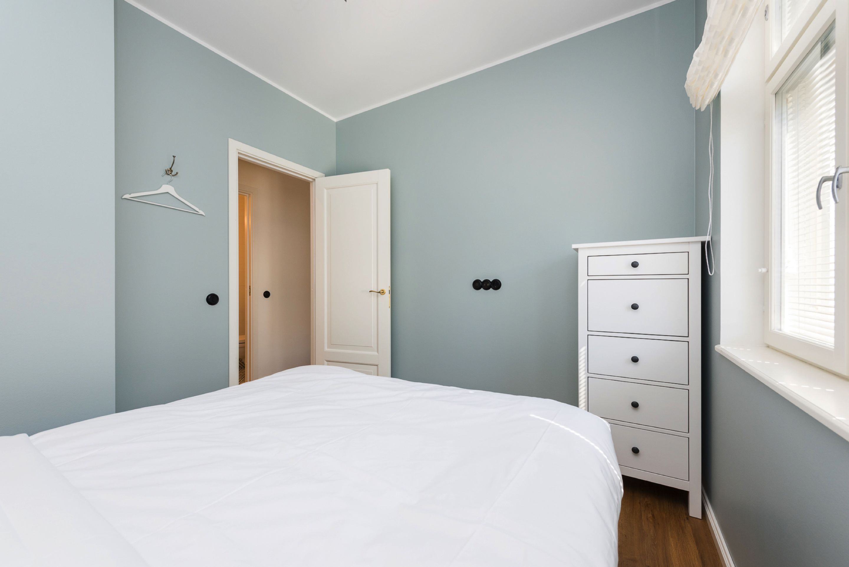 A bedroom with a bed, a dresser, a door, and a window with blinds.