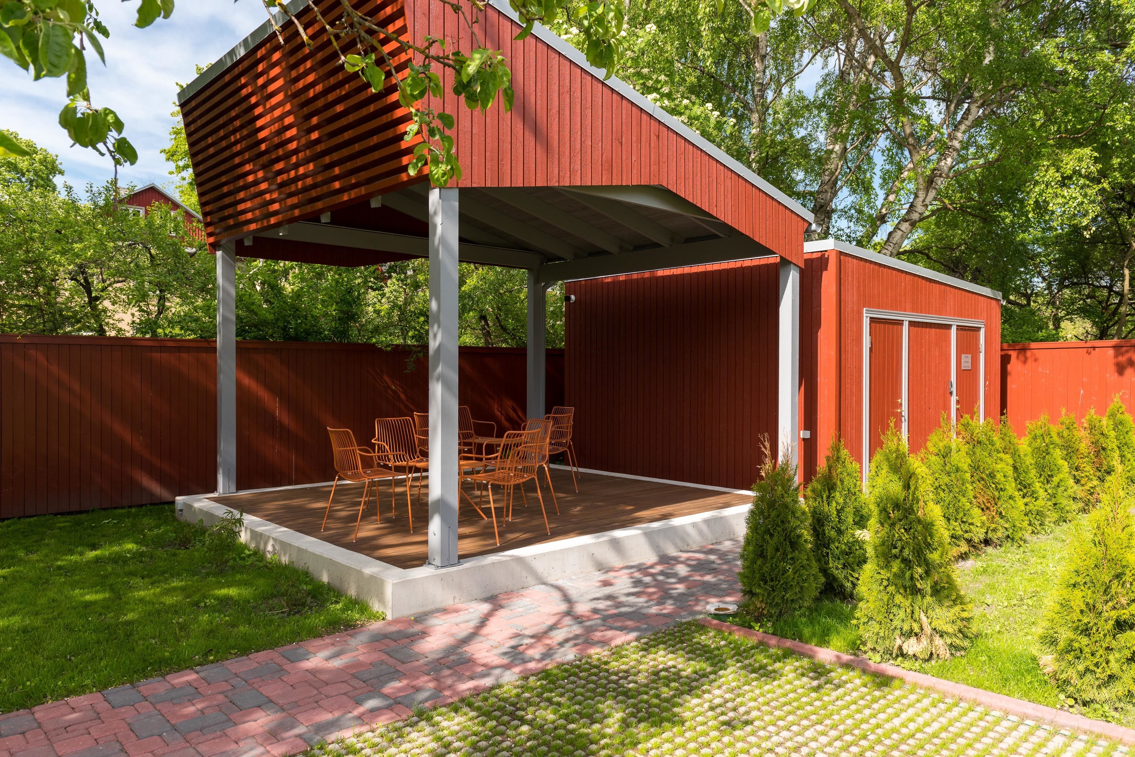 Un patio cubierto con una mesa y sillas, rodeado por un edificio rojo y una valla de madera.