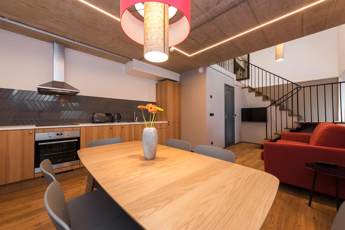 A modern kitchen with a wooden countertop, built-in oven, and a vase with flowers on the dining table.
