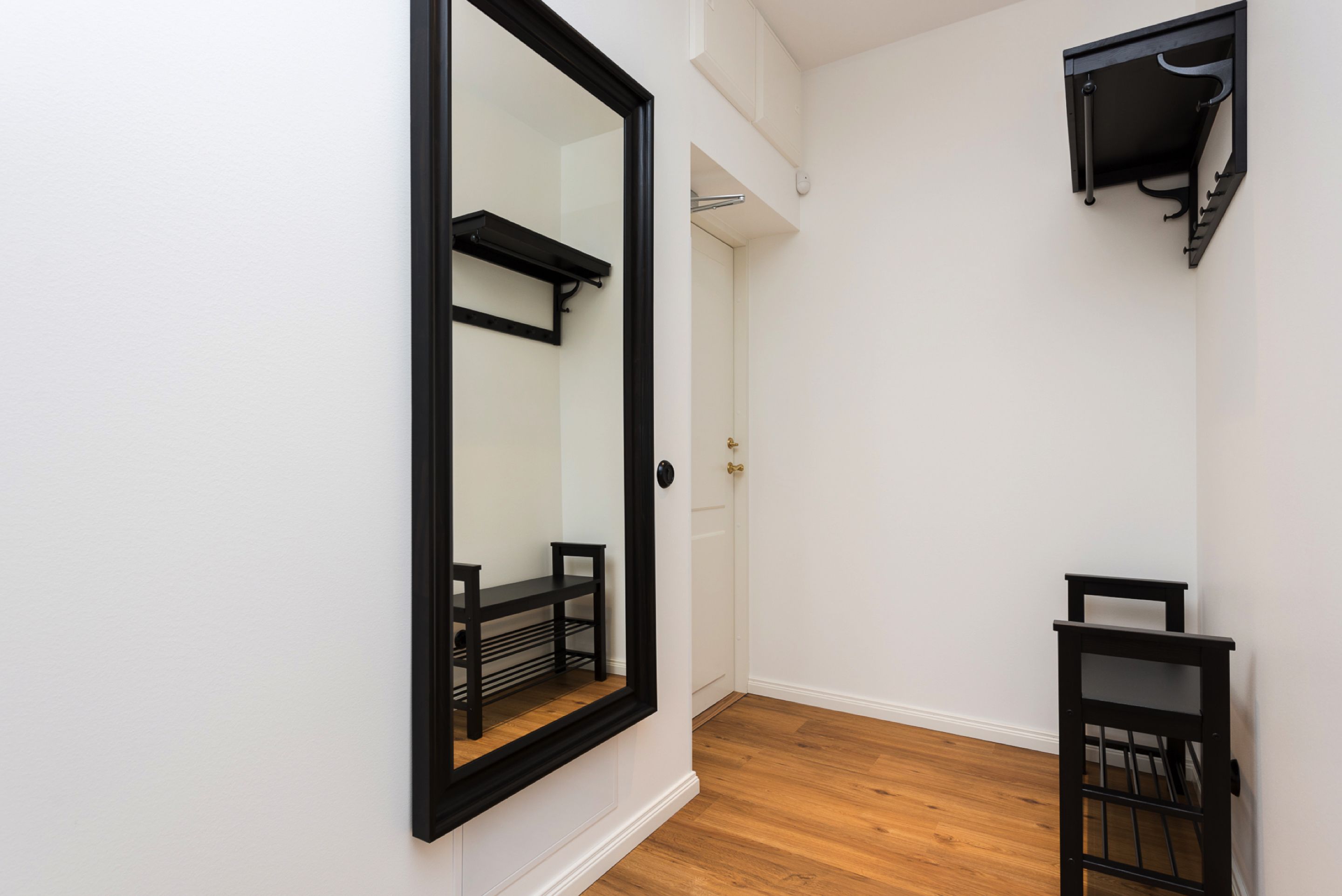 Un couloir étroit avec un grand miroir, une petite table et une étagère noire.