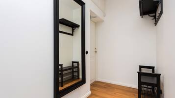 Un couloir étroit avec un grand miroir, une petite table et une étagère noire.