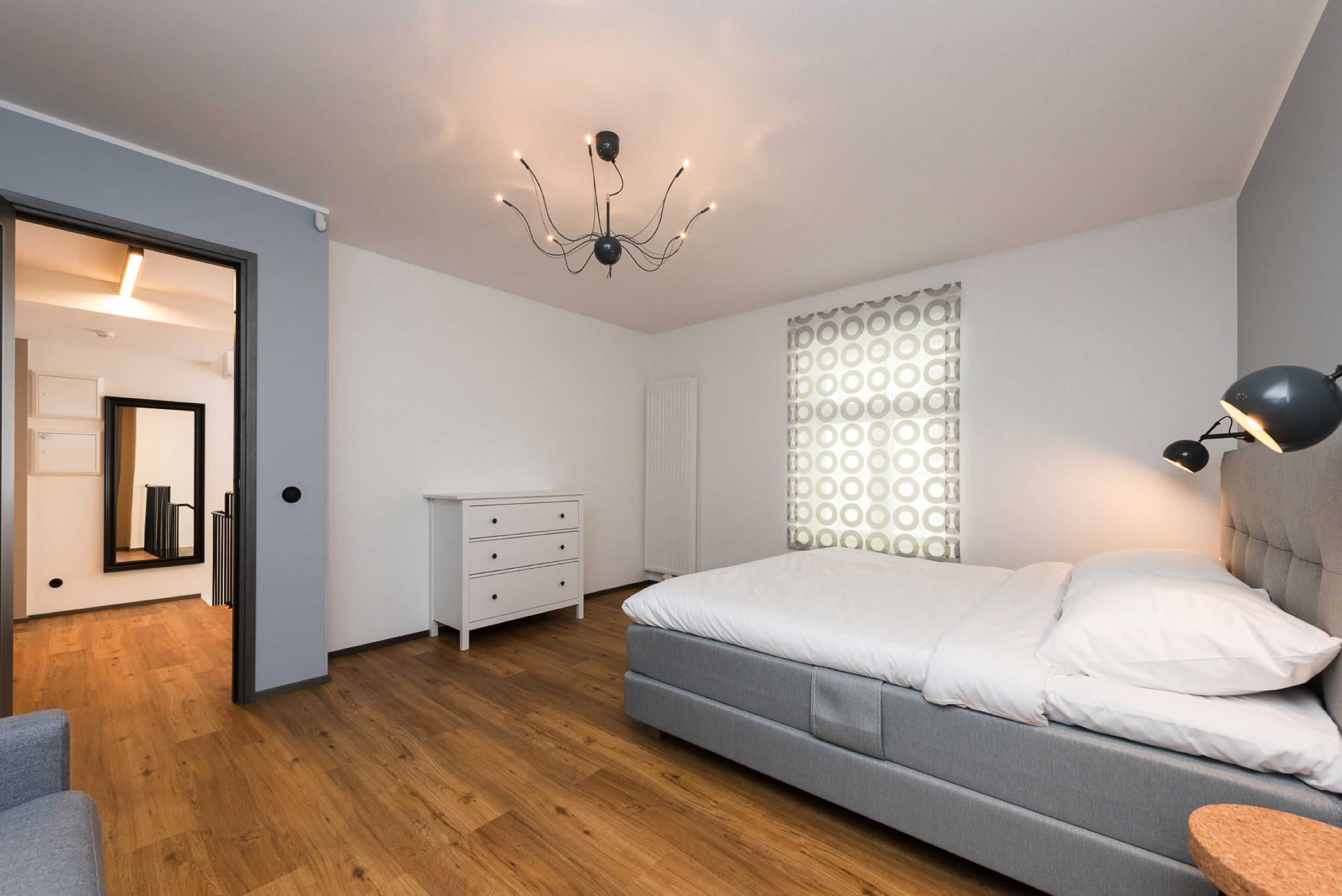Un dormitorio moderno con cama, mesita de noche y una lámpara de araña.