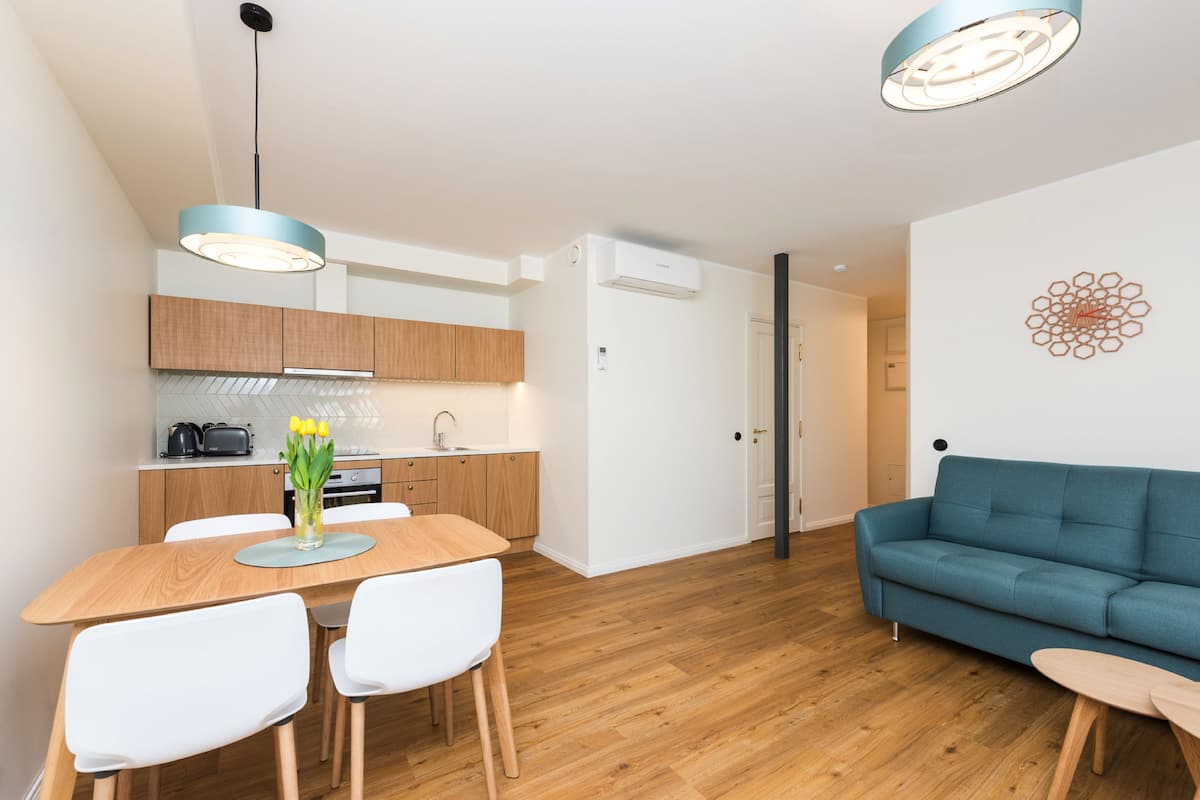 A modern kitchen with wooden cabinets, a dining table with chairs, and a blue sofa in a living area.