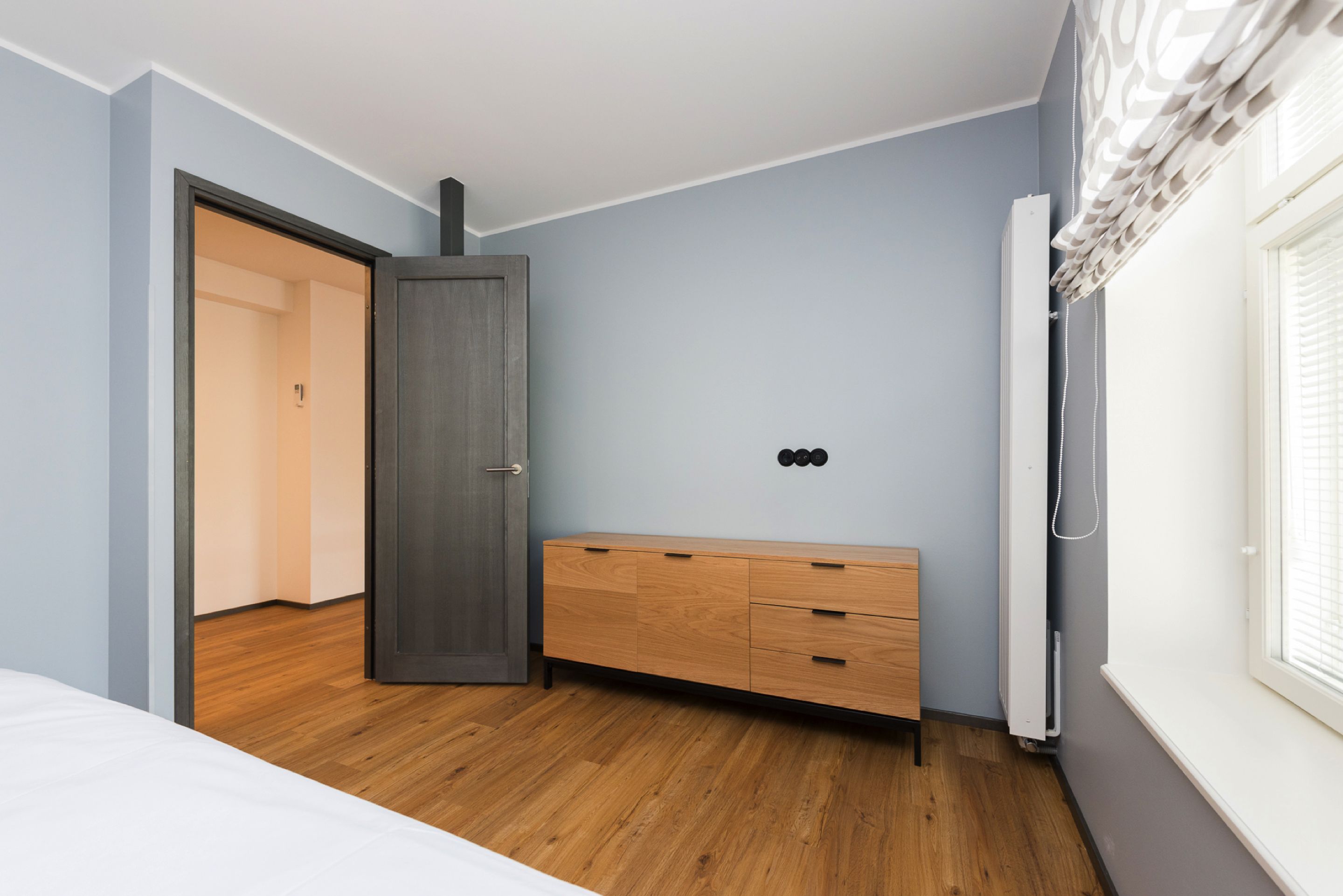 A bedroom with a wooden dresser, a door leading to another room, and a radiator.