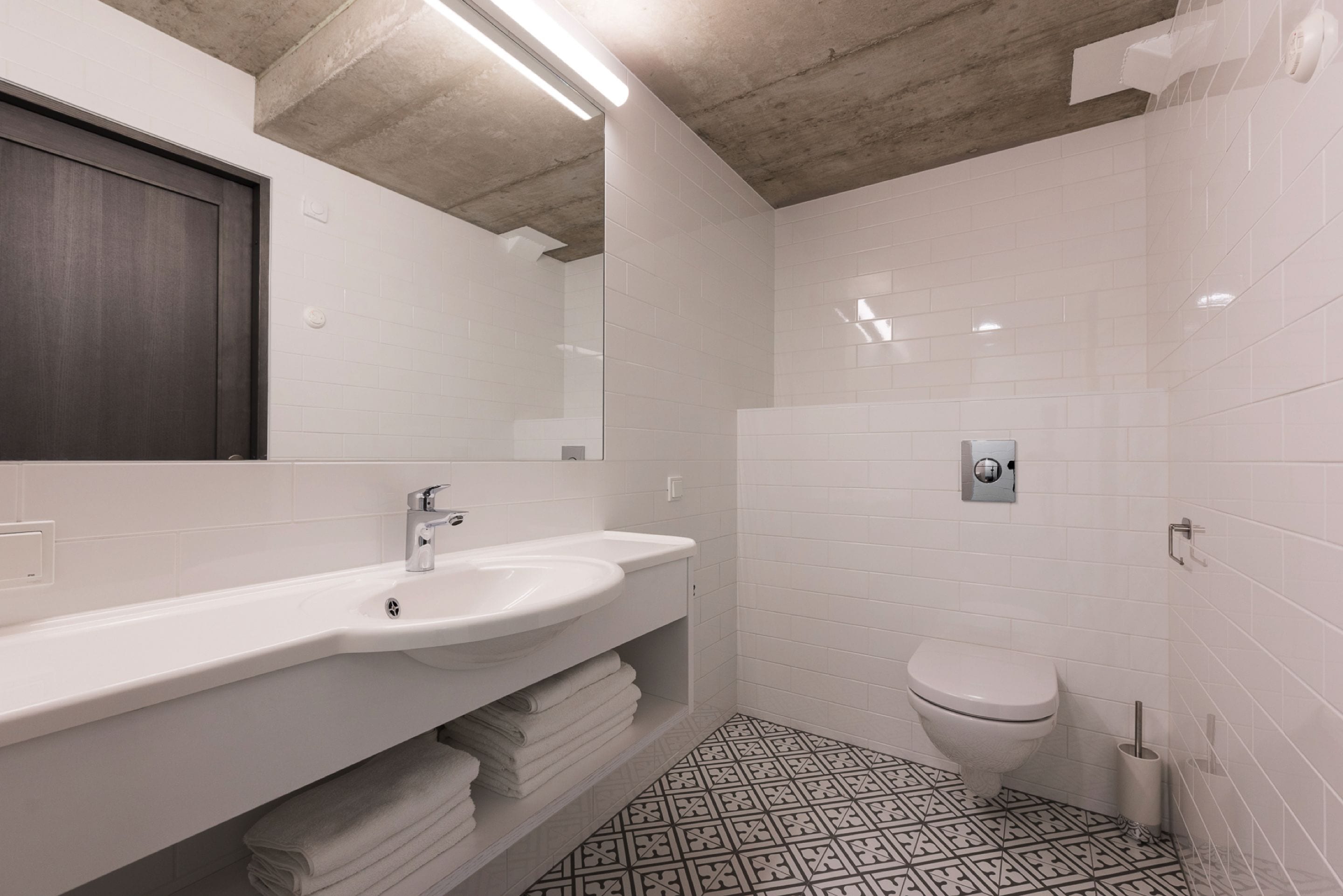 Et moderne badeværelse med en hvid vask, toilet og gulvfliser med et mønster.