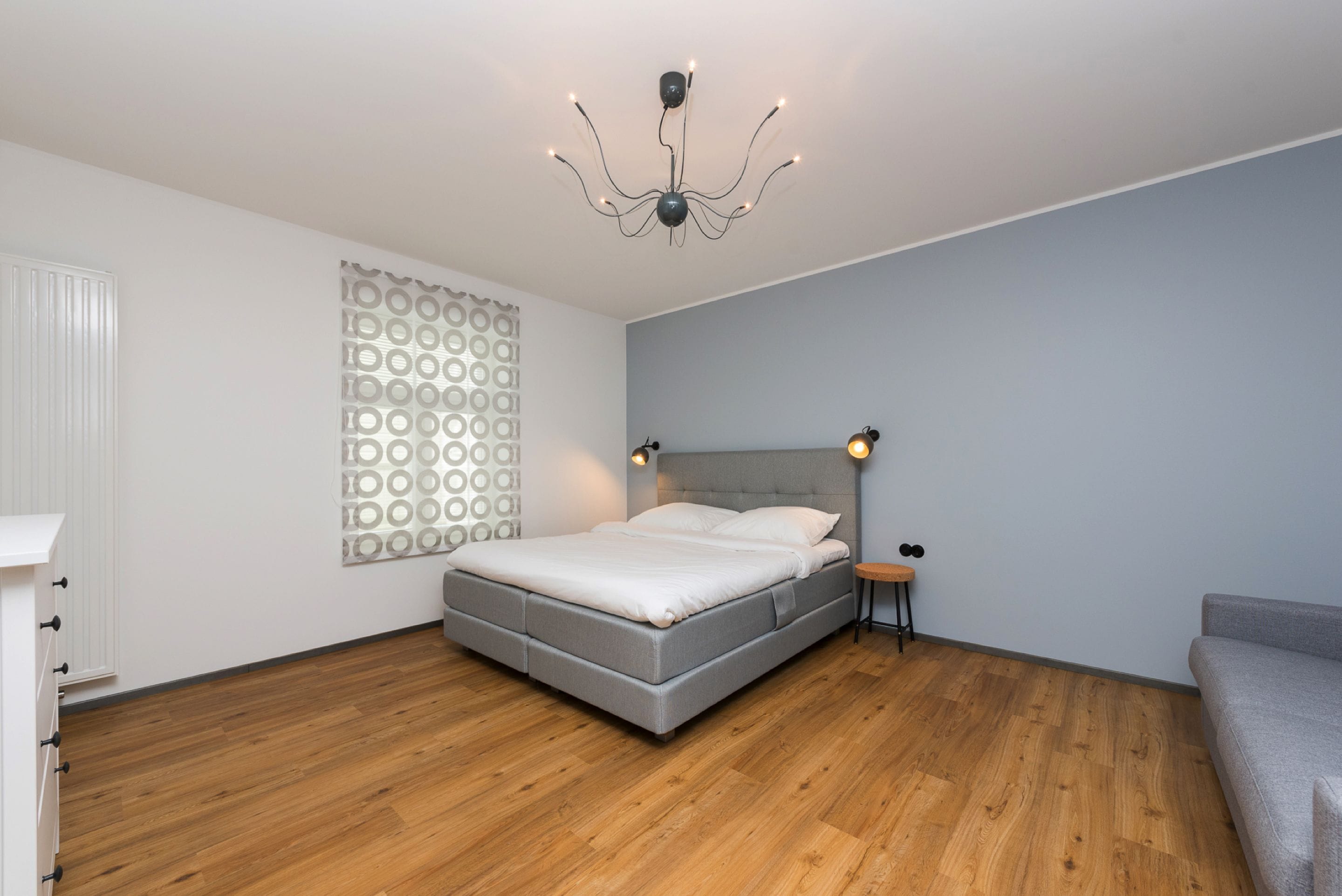 A bedroom with a bed, a bedside table, a wall-mounted light, and a patterned wall.