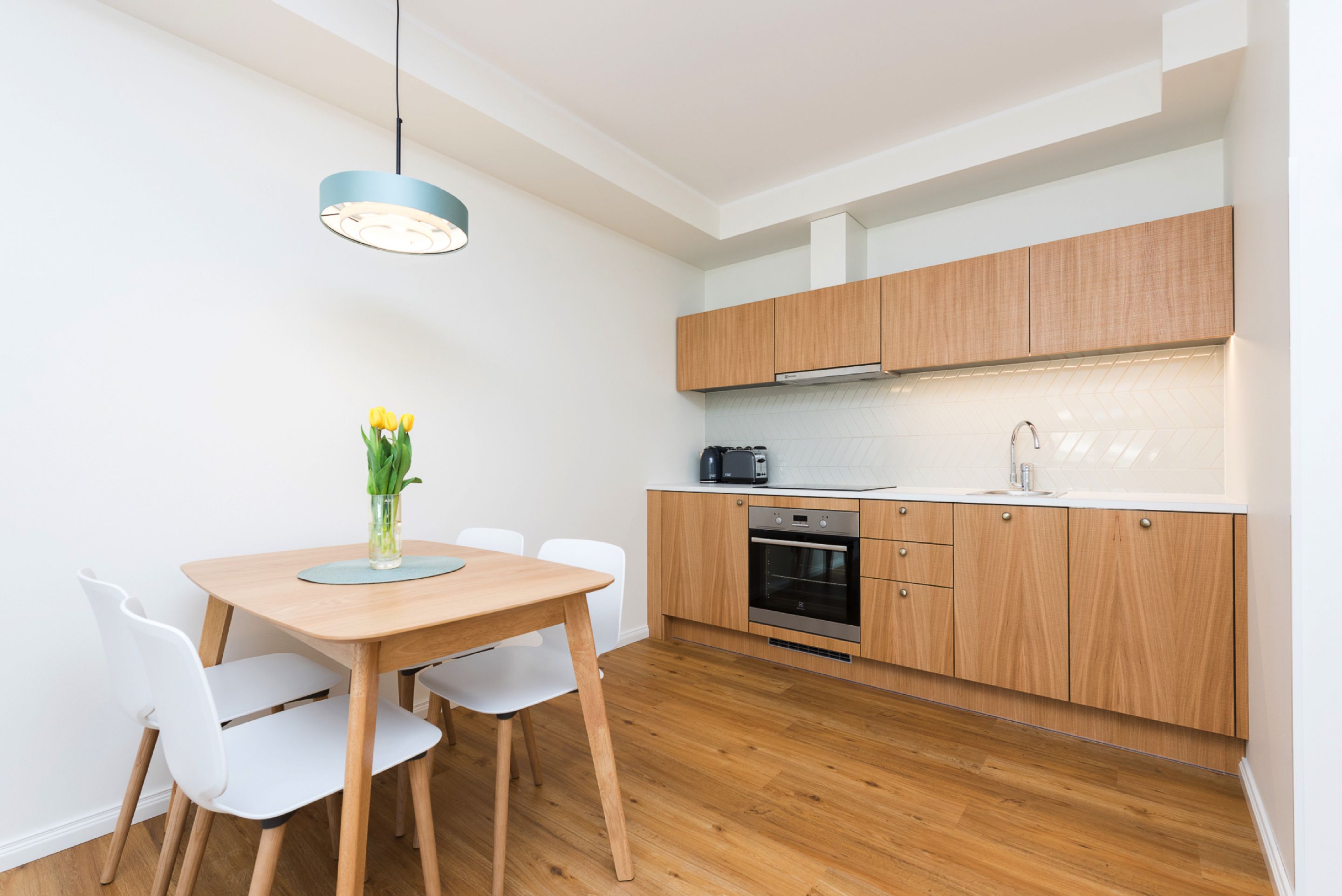 Una cocina moderna con armarios de madera, horno empotrado y un comedor con mesa y sillas.