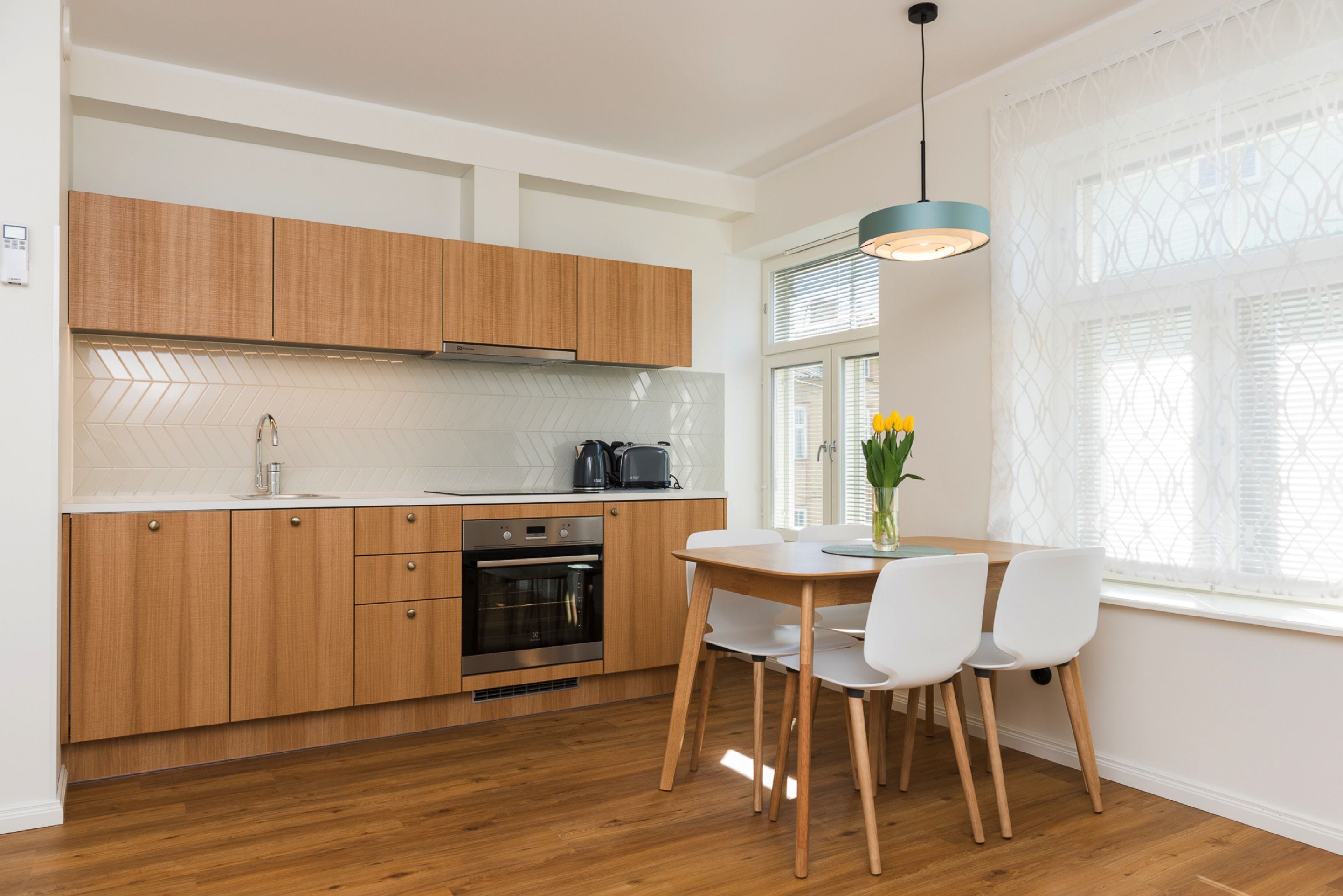 A modern kitchen with wooden cabinets, a built-in oven, and a dining area with a table and chairs.