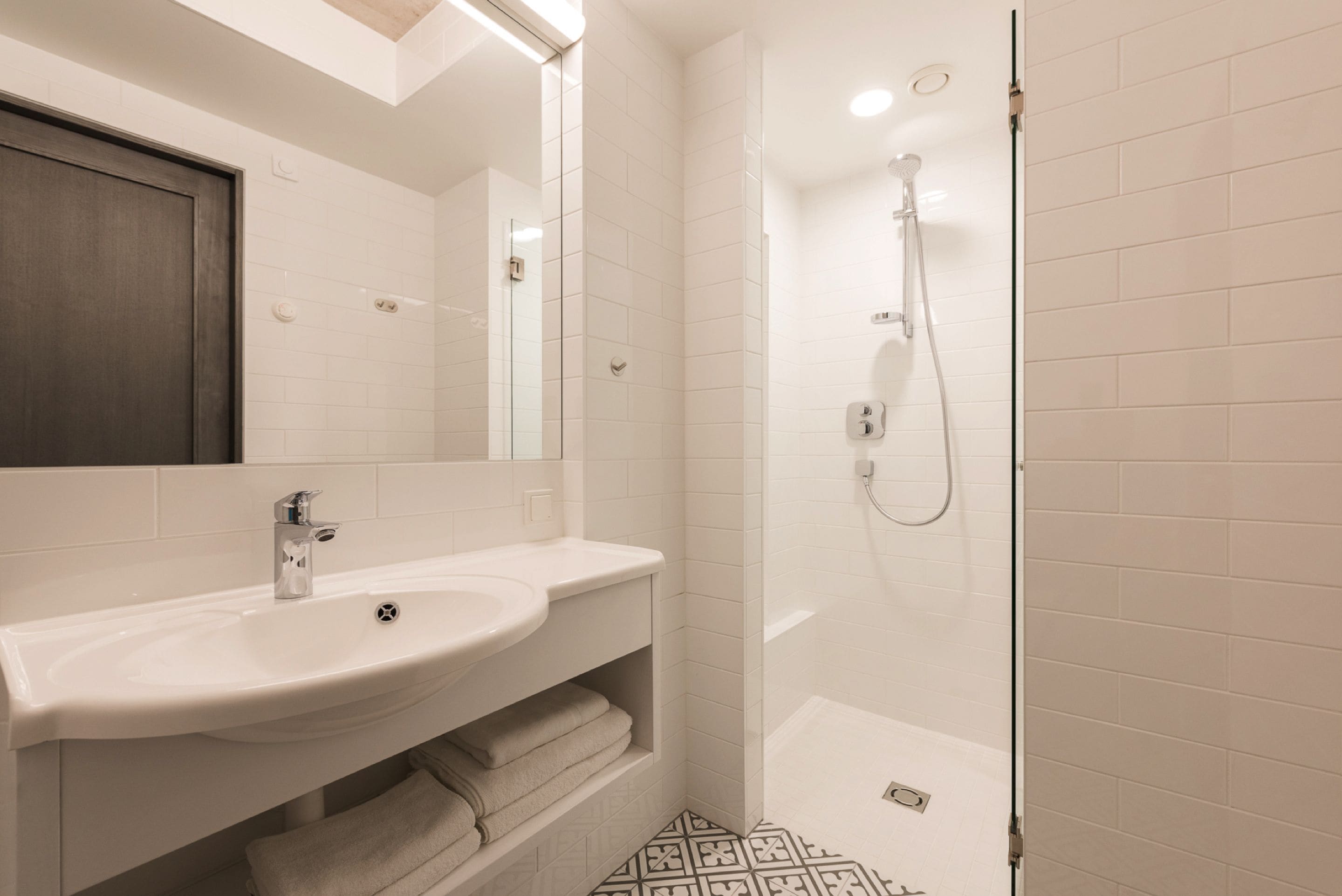 A modern bathroom with a white sink, mirror, and shower.
