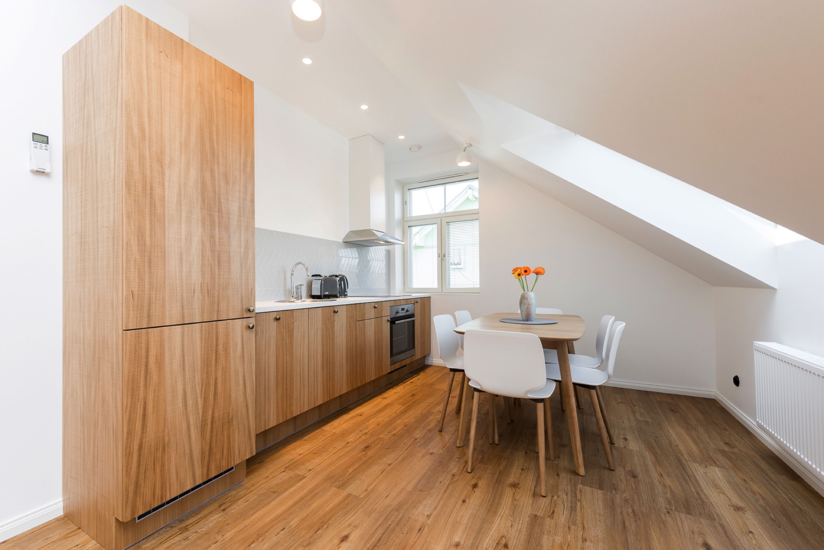 Eine moderne Küche mit Holzausbau, einem Esstisch mit Stühlen und einem Fenster, das für natürliches Licht sorgt.