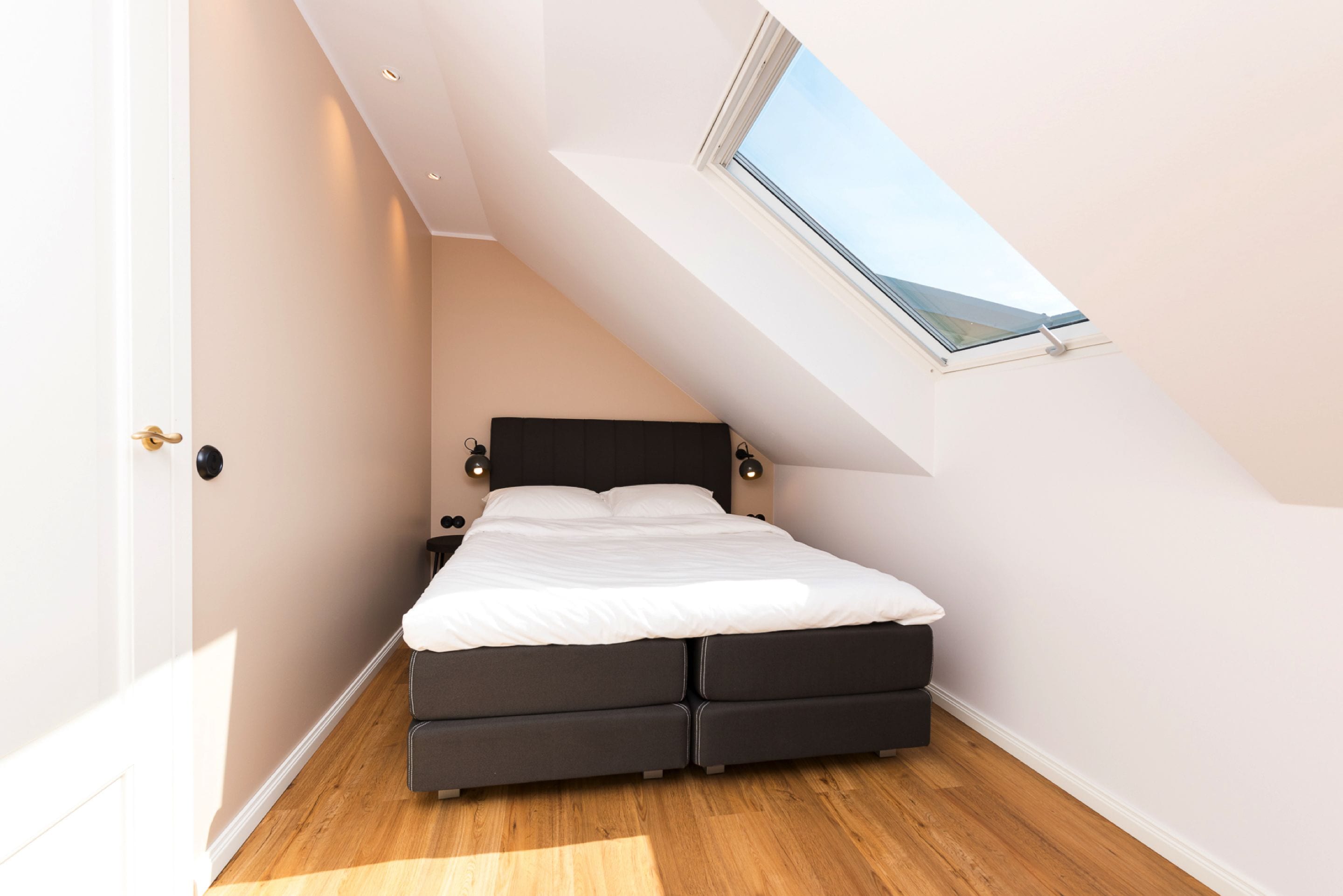 Un dormitorio con tragaluz, cama con dos cajones y mesita de noche.