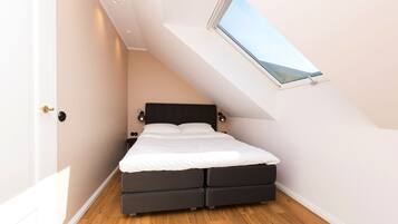 Un dormitorio con tragaluz, cama con dos cajones y mesita de noche.