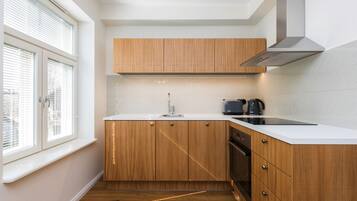 Una cocina compacta con armarios de madera, una encimera blanca, un extractor de acero inoxidable y una ventana con persianas.