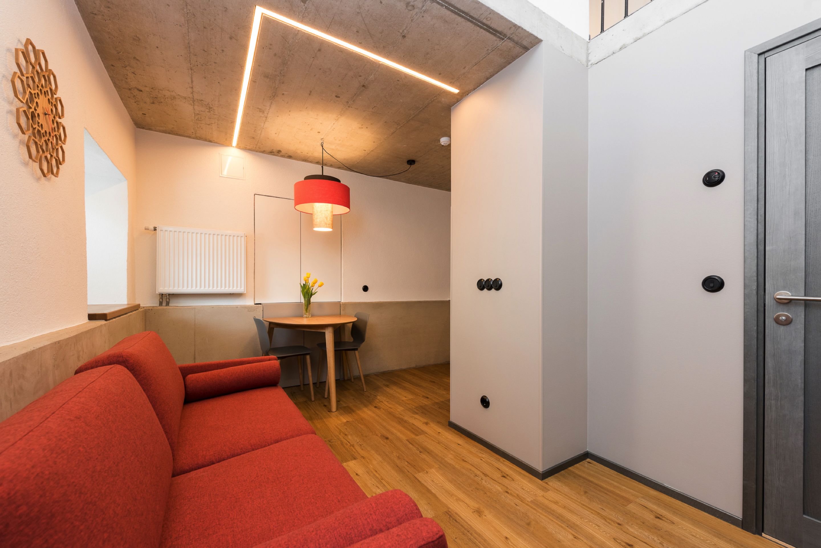 A modern room with a red sofa, a small table with a vase, and a pendant light.