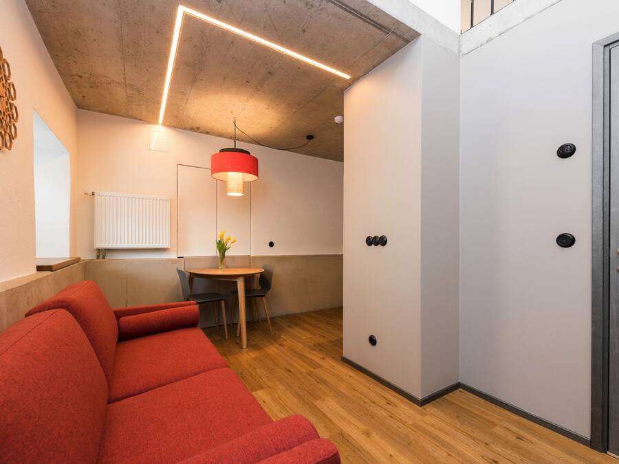 Habitació moderna amb un sofà vermell, una taula petita amb un ram i una làmpada penjant.