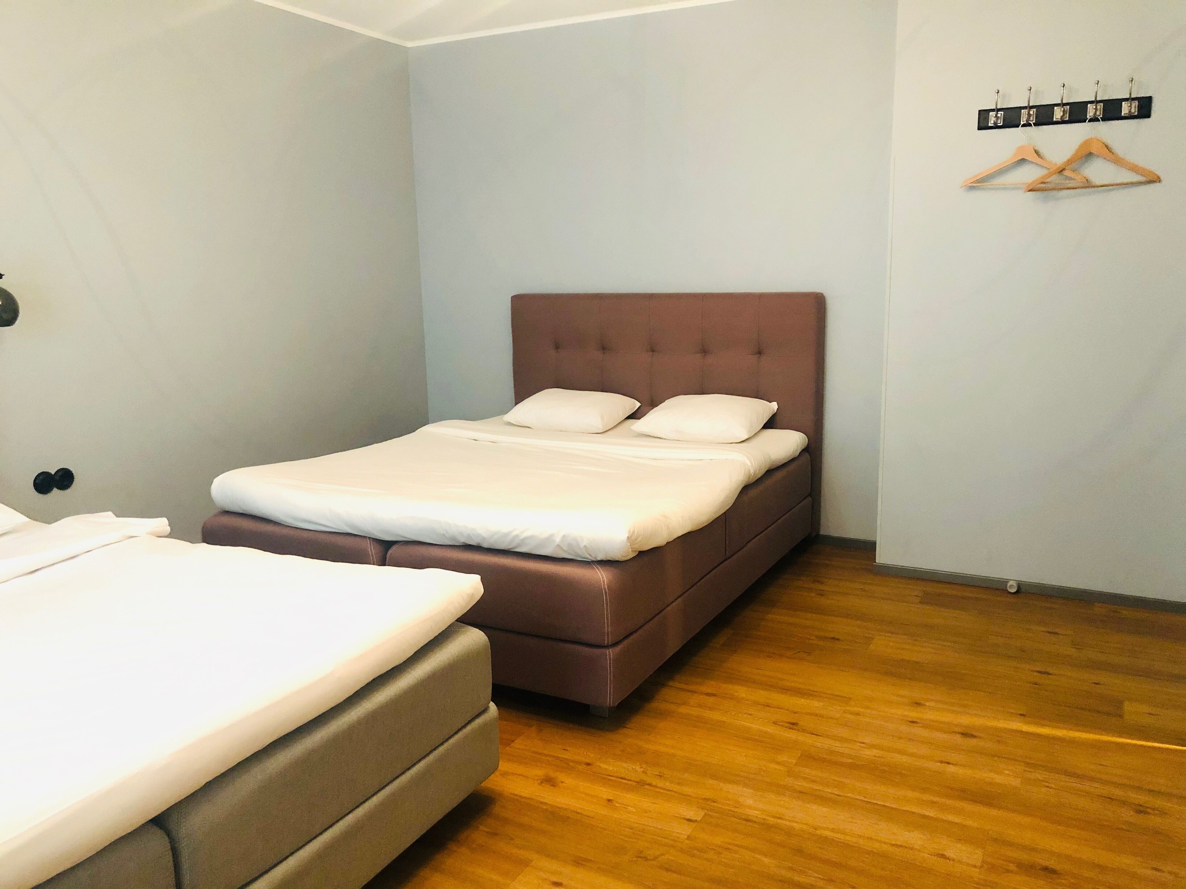A bedroom with a bed, a smaller bed, wooden flooring, and a coat rack with hangers.