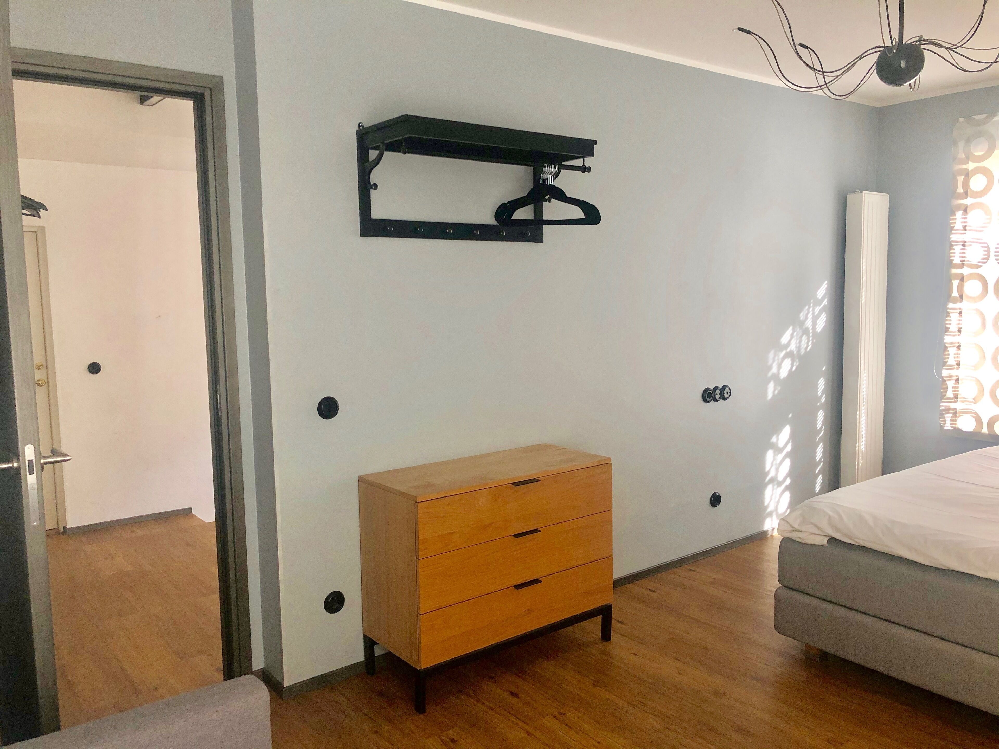 A bedroom with a wooden dresser, a bed, and a wall-mounted shelf.
